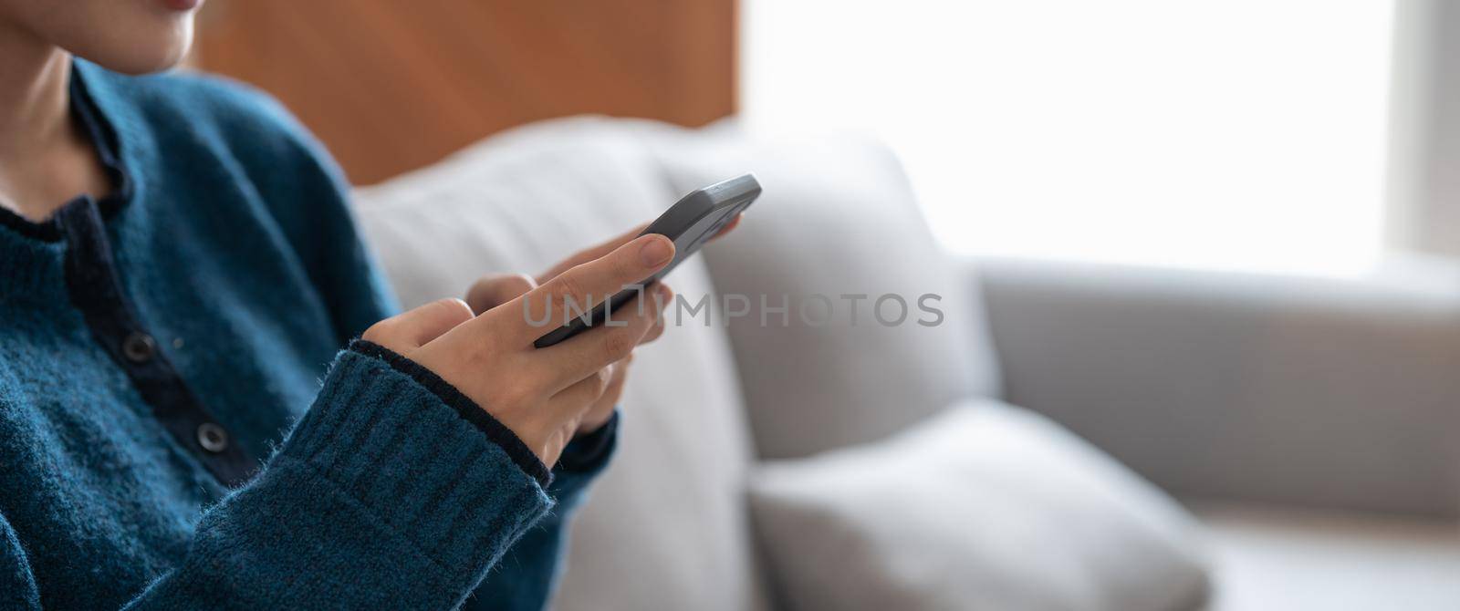 Close up of a woman using mobile smart phone on sofa at cozy home.