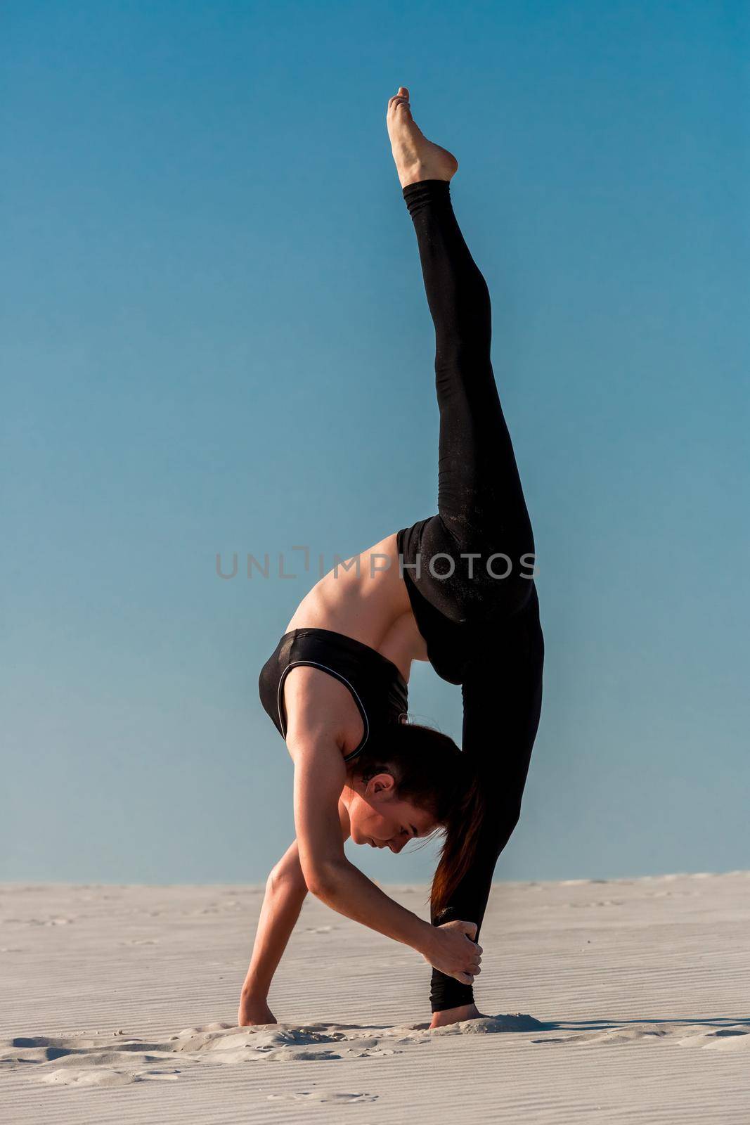 Side view of concentrated fit brunette performing leg and glute workout, doing squats in studio on grey background. Fitness concept