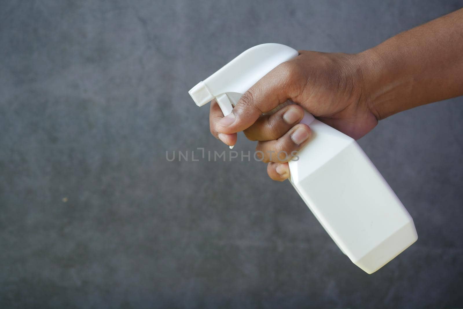 holding white color spray bottle with copy space against black background .