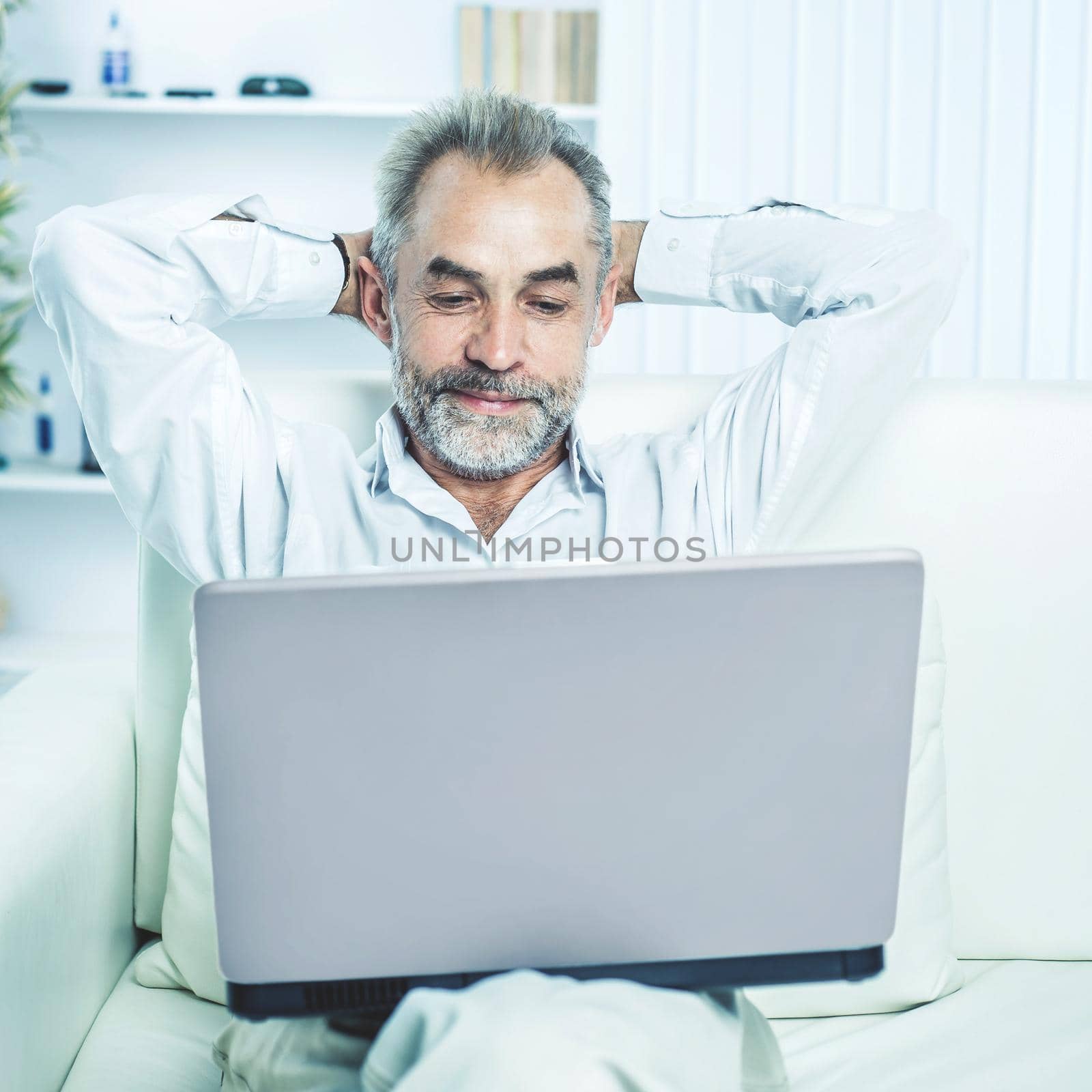 successful businessman working on laptop sitting on sofa in modern office. by SmartPhotoLab