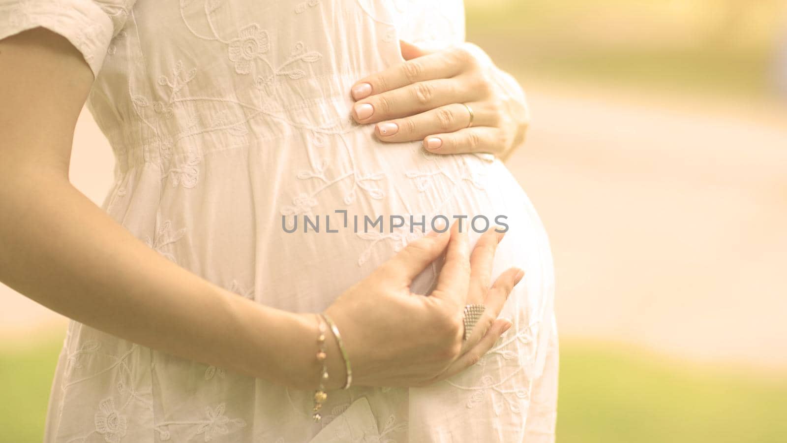 Image of pregnant woman touching her belly with hands on a bright sunny day