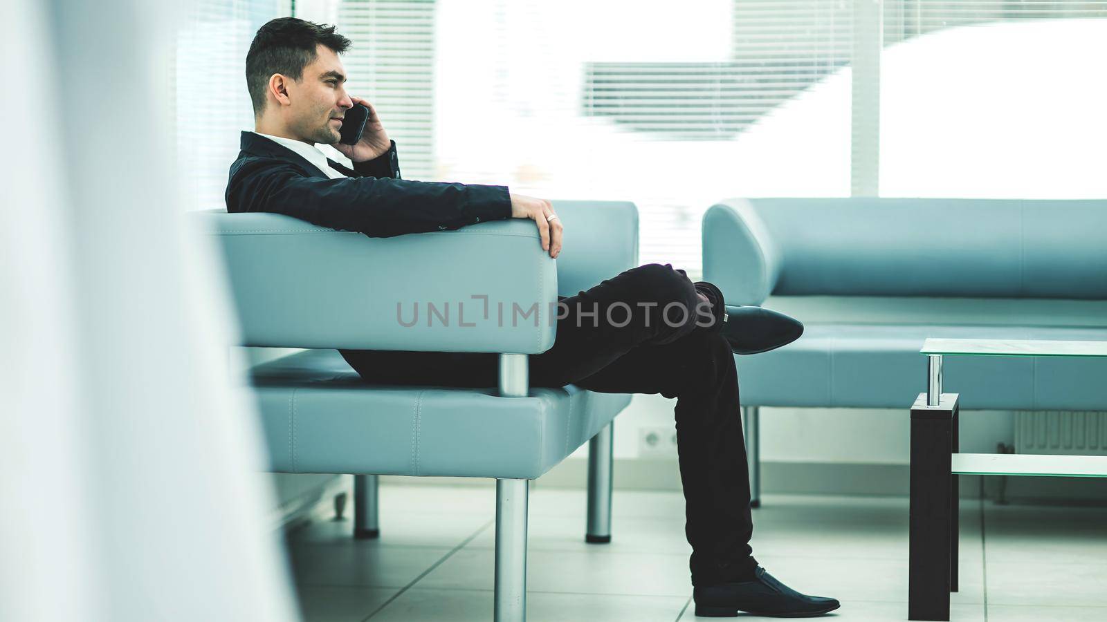 businessman sits in the lobby of a modern office and talking on the phone.the photo has a empty space for your text
