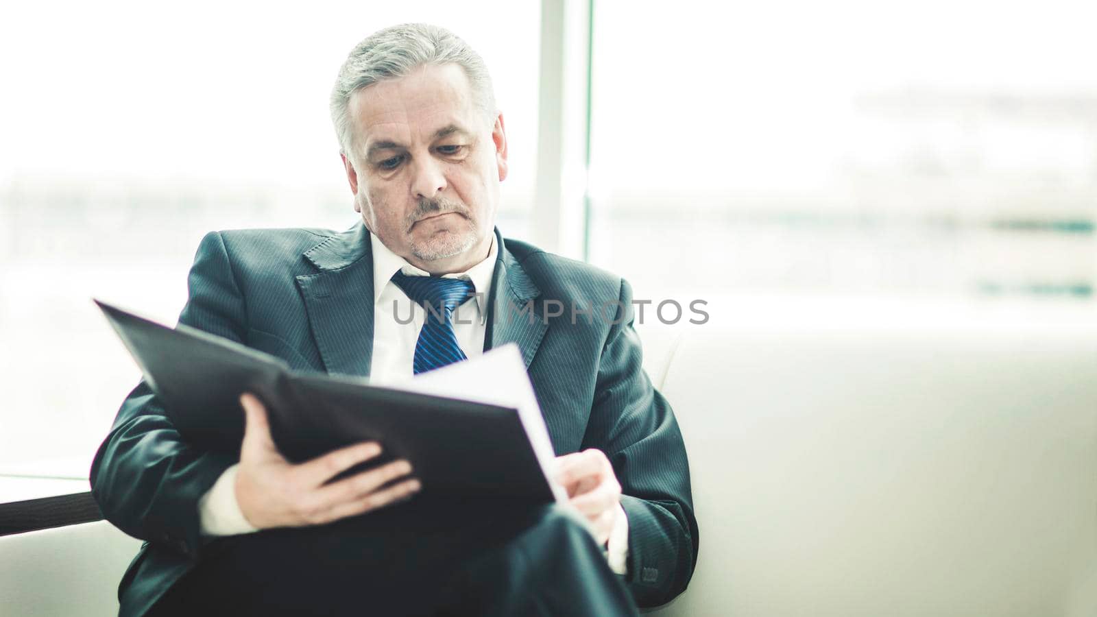 experienced businessman studies working papers sitting on a white sofa in a private office