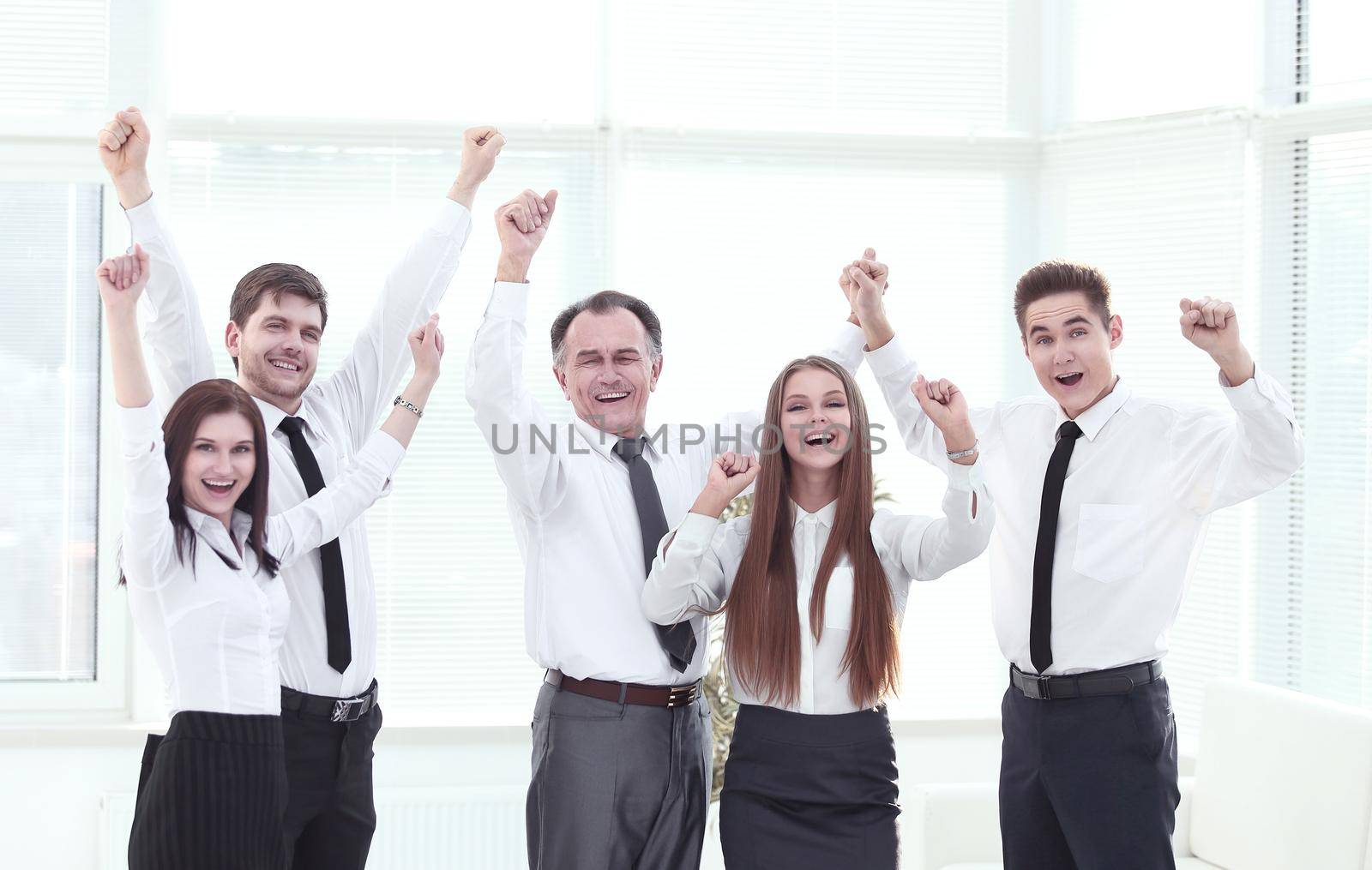 group of happy young people in formal wear celebrating, gesturing, keeping arms raised and expressing positivity.