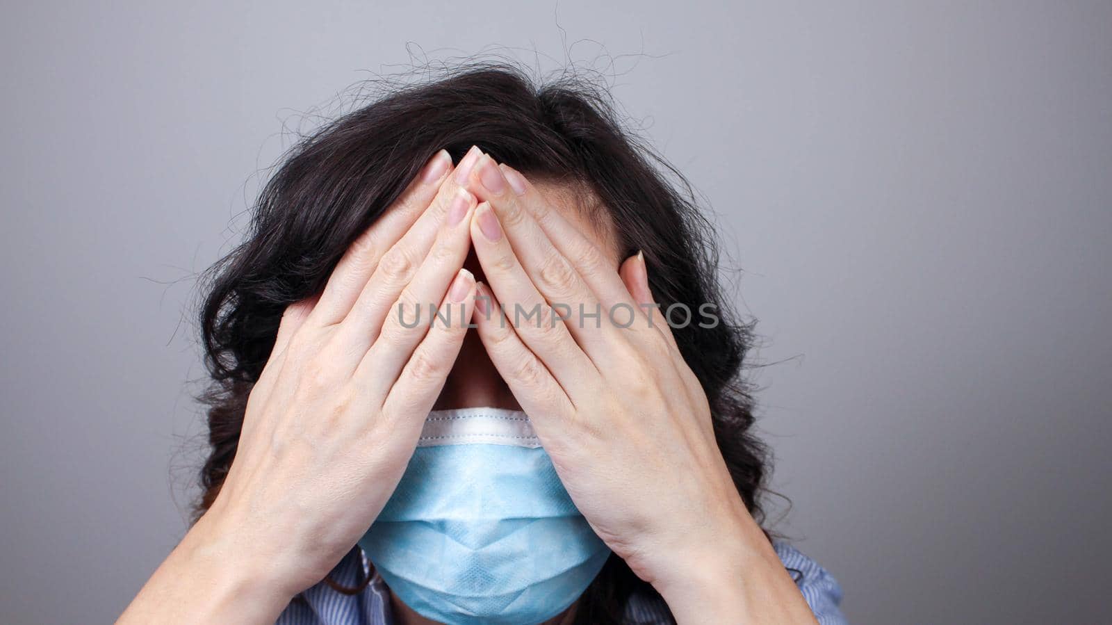 Woman wearing protection face mask against coronavirus covering her eyes with hands. Woman in a mask hiding her eyes. by JuliaDorian