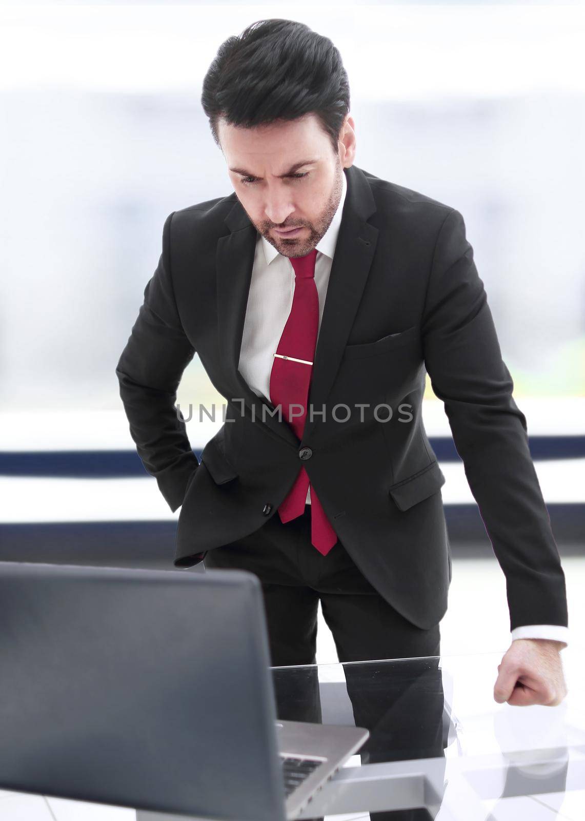 Businessman standing at his Desk and looking at the laptop screen by asdf