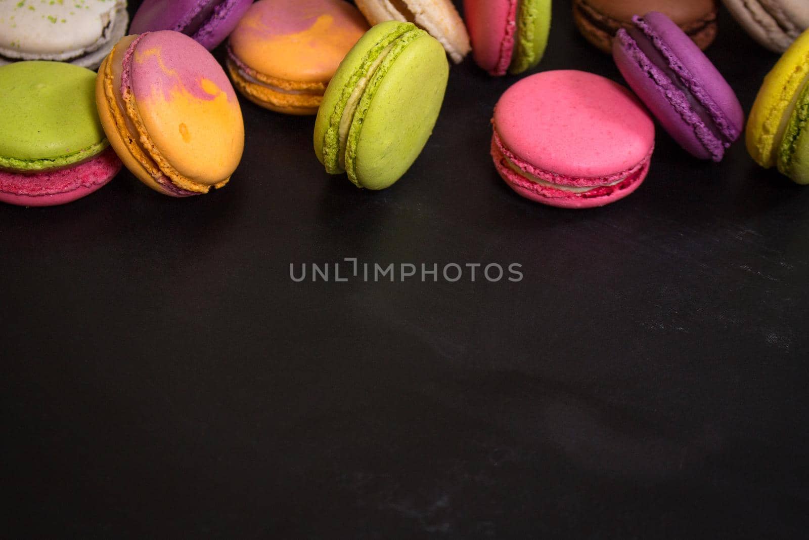 Assorted colorful french cookies macaroons on a black background. Space for text. Closeup. Top view. Concept of the baking macaroons