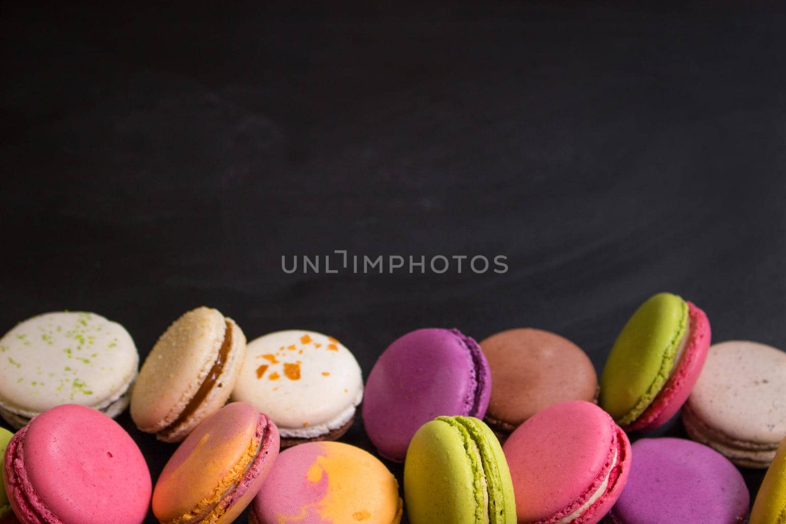 Assorted colorful french cookies macarons on a black background. Space for text. Closeup. Top view. Concept of the baking macarons