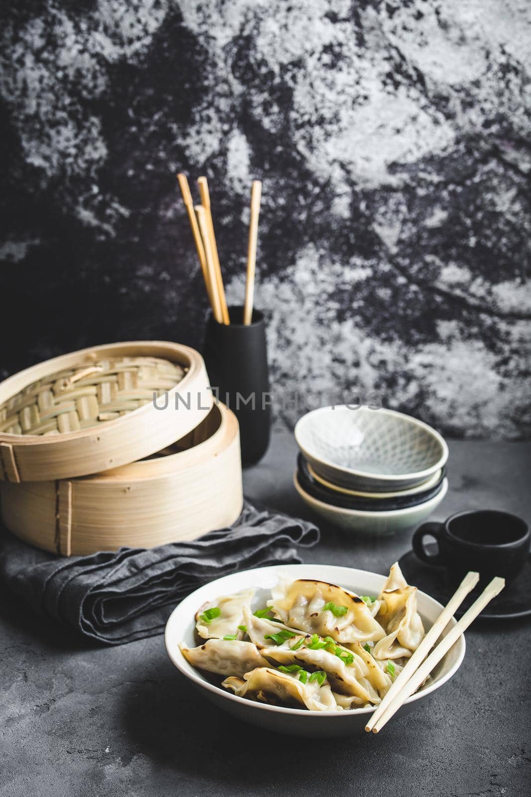 Asian dumplings in bowl, chopsticks, bamboo steamer, plates. Asian table setting. Chinese dumplings for dinner. Selective focus. Asian style decoration. Chinese fresh homemade food. Closeup