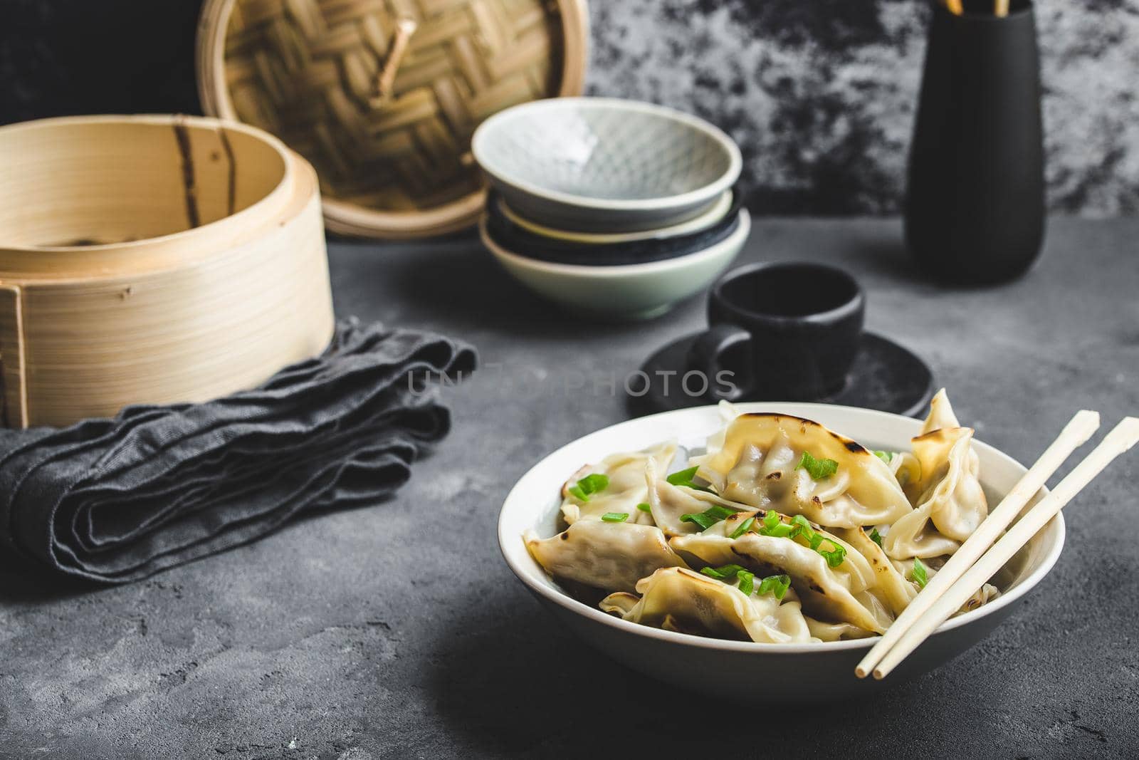 Asian dumplings in bowl, chopsticks, bamboo steamer, plates. Asian table setting. Chinese dumplings for dinner. Selective focus. Asian style decoration. Chinese fresh homemade food. Closeup