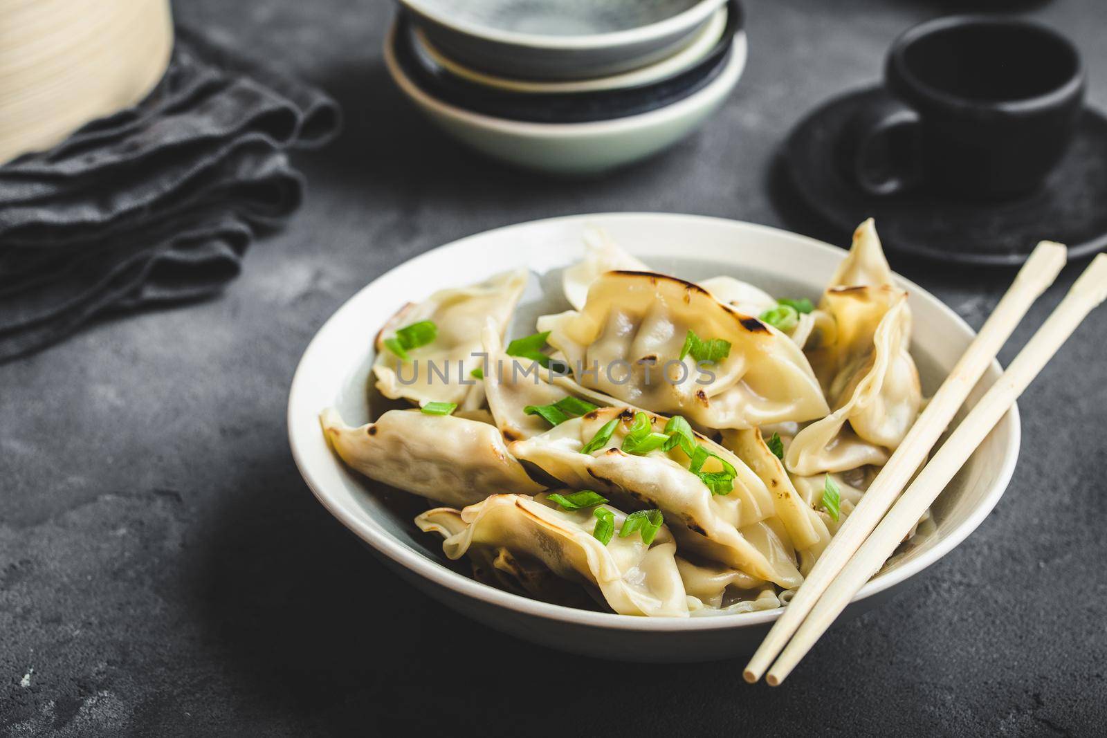 Asian dumplings in bowl, chopsticks, bamboo steamer, plates. Asian table setting. Chinese dumplings for dinner. Selective focus. Asian style decoration. Chinese fresh homemade food. Closeup