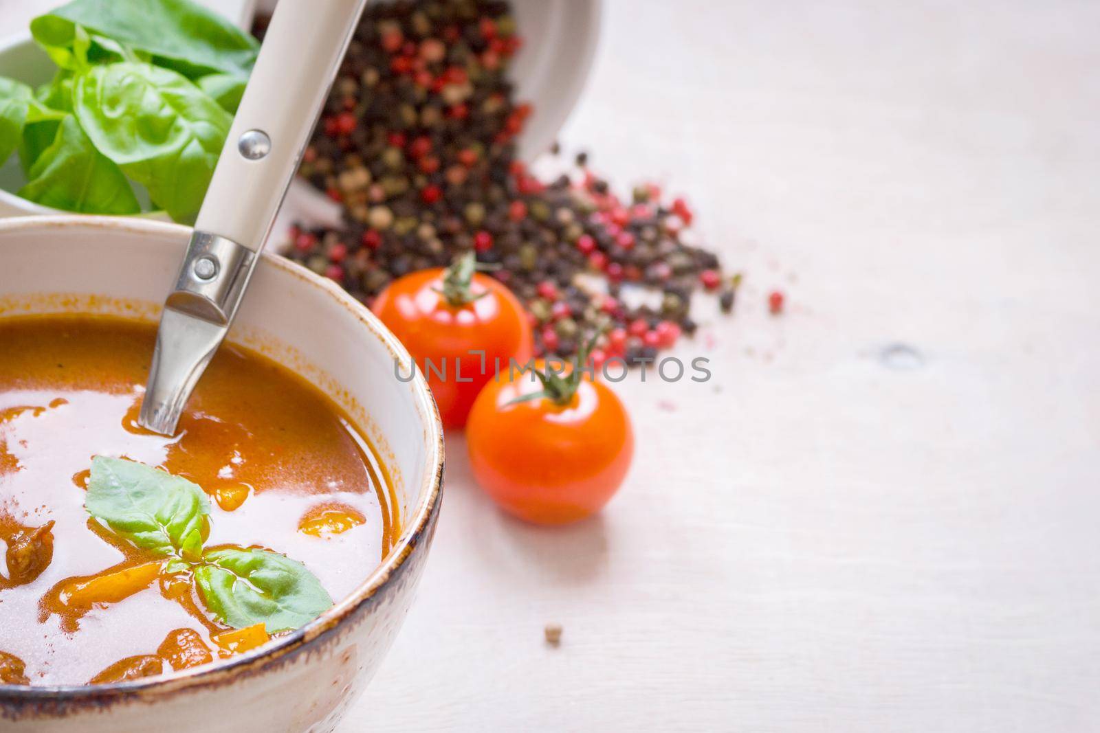 Tomato soup with meat on a white rustic wooden table with fresh cherry tomatoes, basil, dry pepper and red gingham kitchen towel. Ingredients for soup. Soup background. Space for text