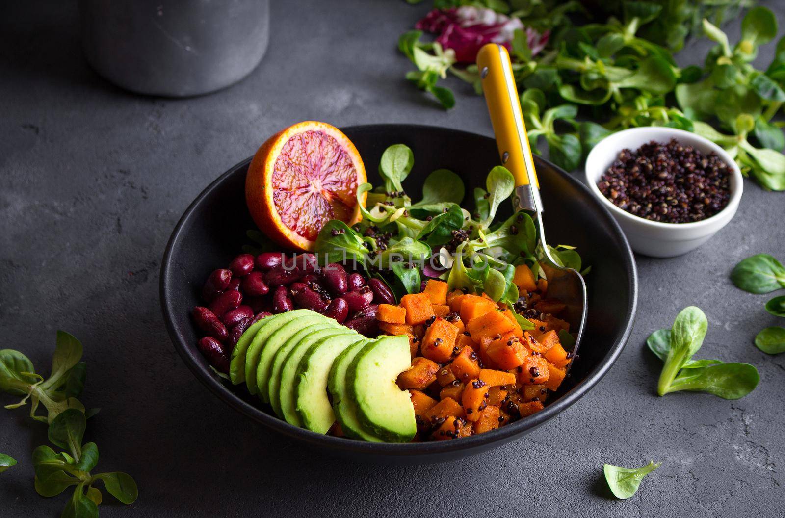 Quinoa salad in bowl with avocado, sweet potato, beans, herbs, orange on concrete rustic background. Quinoa superfood concept. Clean healthy detox eating. Vegan/vegetarian food. Making healthy salad