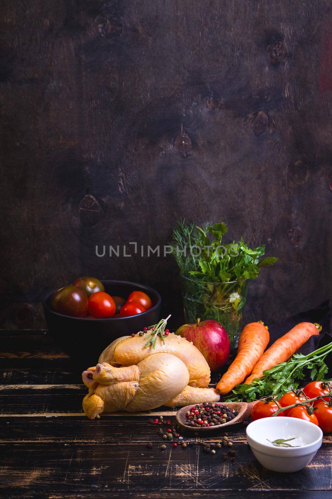Raw whole chicken ready for cooking. Chicken, vegetables, herbs, spices on black rustic wooden background. Space for text. Food frame. Diet or healthy eating. Ingredients for cooking. Selective focus