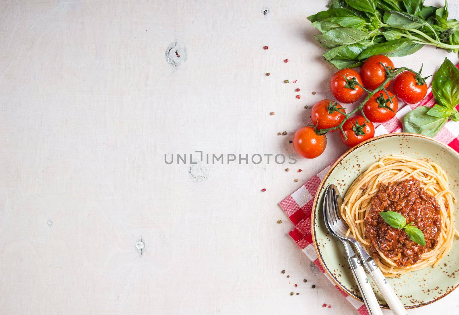 Italian pasta bolognese. Spaghetti with meat and tomato sauce in a plate with Italian tablecloth on a wooden white background. With fresh cherry tomatoes, basil. Food frame. Space for text. Top view