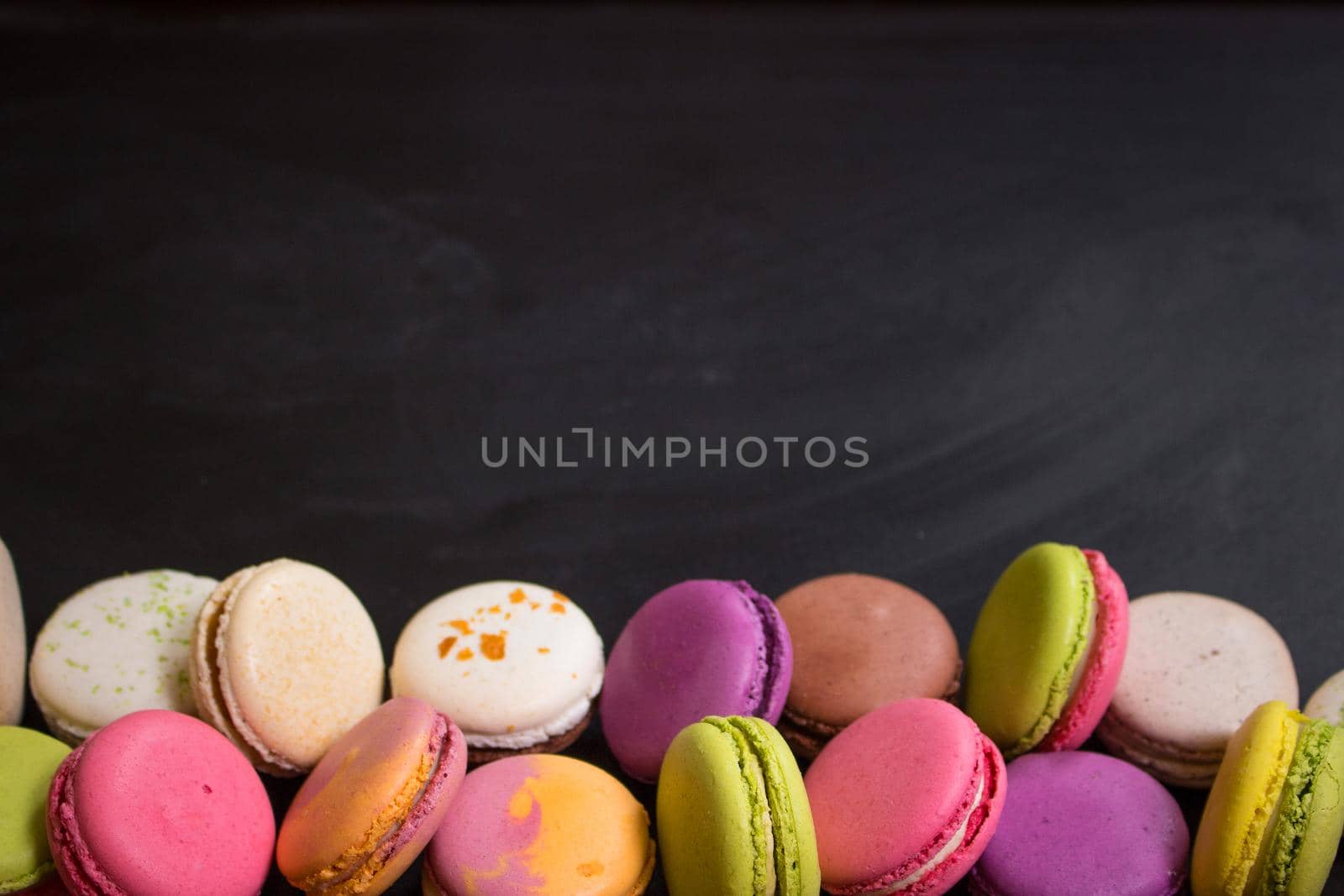 Assorted colorful french cookies macarons on a black background. Space for text. Closeup. Top view. Concept of the baking macarons