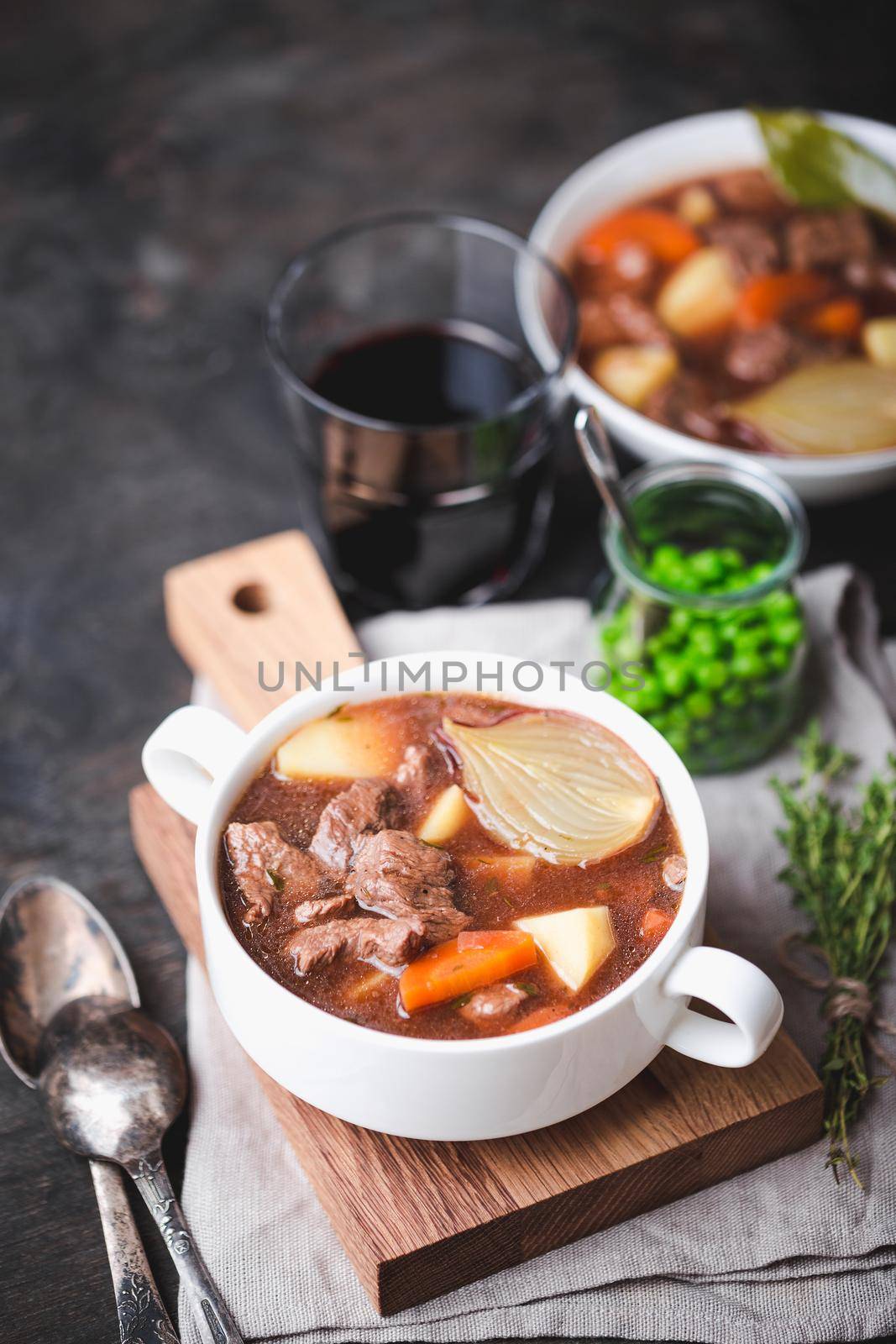 Meat stew with beef, potato, carrot, onion, spices, green peas. Slow cooked meat stew, bowl, wooden background. Hot autumn/winter dish. Selective focus. Comfort food. Homemade soup/ragout/casserole