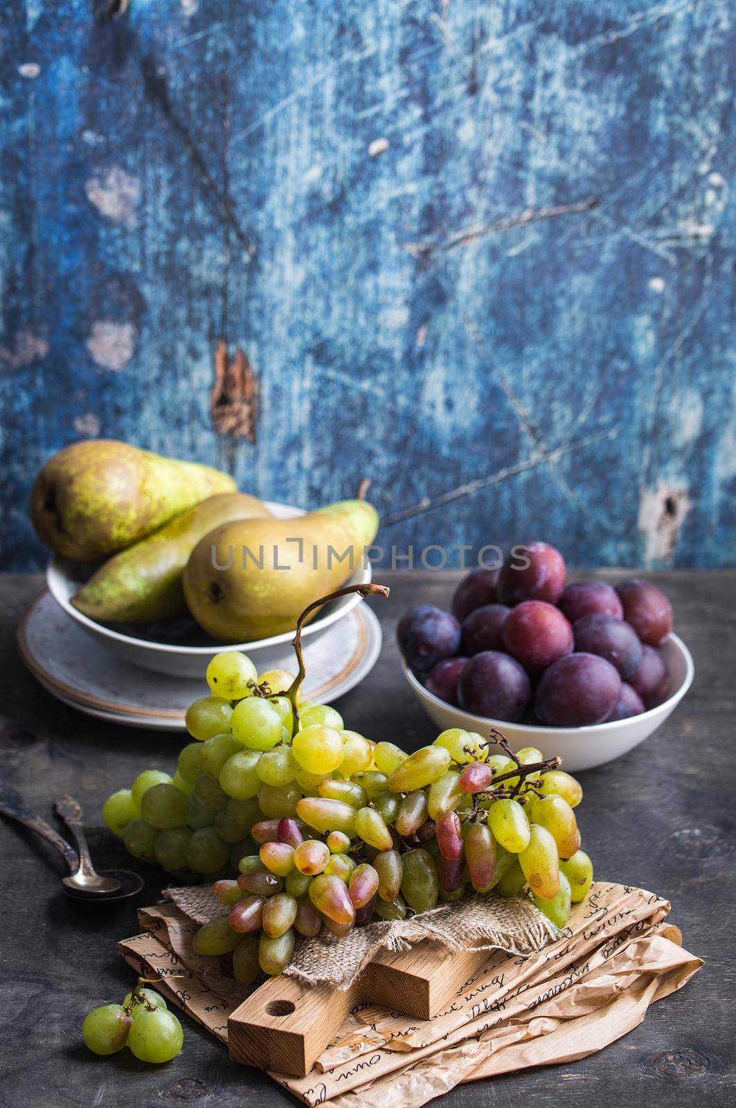 Fresh ripe grapes on wooden cutting board, pears and plums in bowls, wooden rustic background. Fresh juicy organic fruits. Close up. Organic natural fruits. Autumn/fall setting. Harvest/crop/garden
