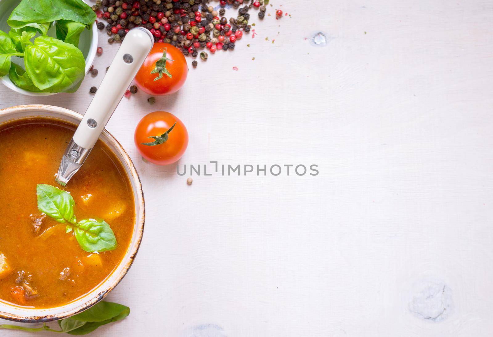 Tomato soup with meat on a white rustic wooden table with fresh cherry tomatoes, basil, dry pepper and red gingham kitchen towel. Ingredients for soup. Soup background. Space for text