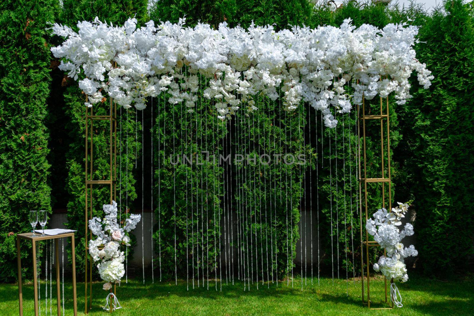 White wedding arch on a background of evergreen thuja. Summer wedding ceremony in the park.