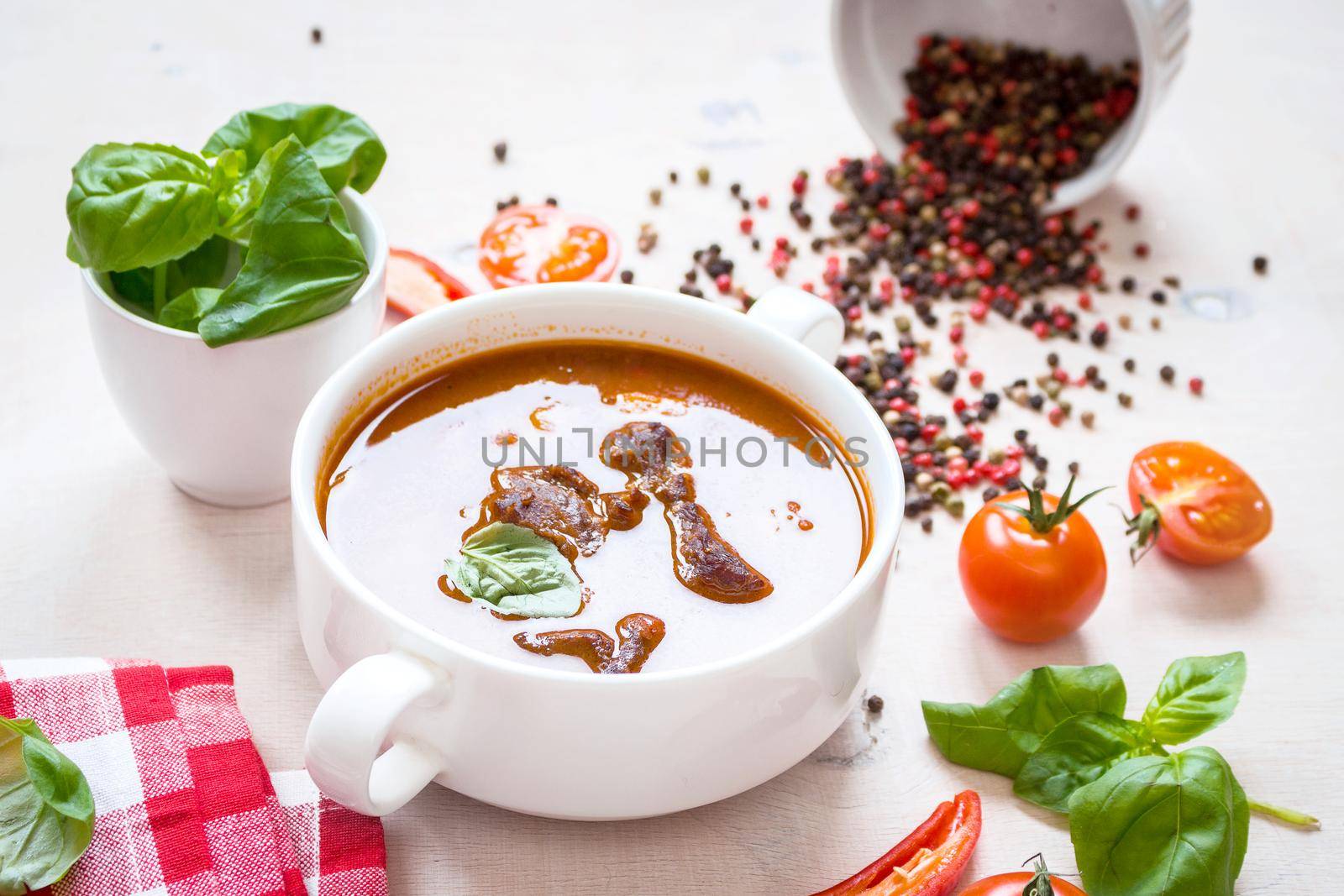 Delicious tomato soup with meat on a white rustic wooden table with fresh cherry tomatoes, basil leaves, cut chili pepper and red gingham kitchen towel. Ingredients for soup. Top view