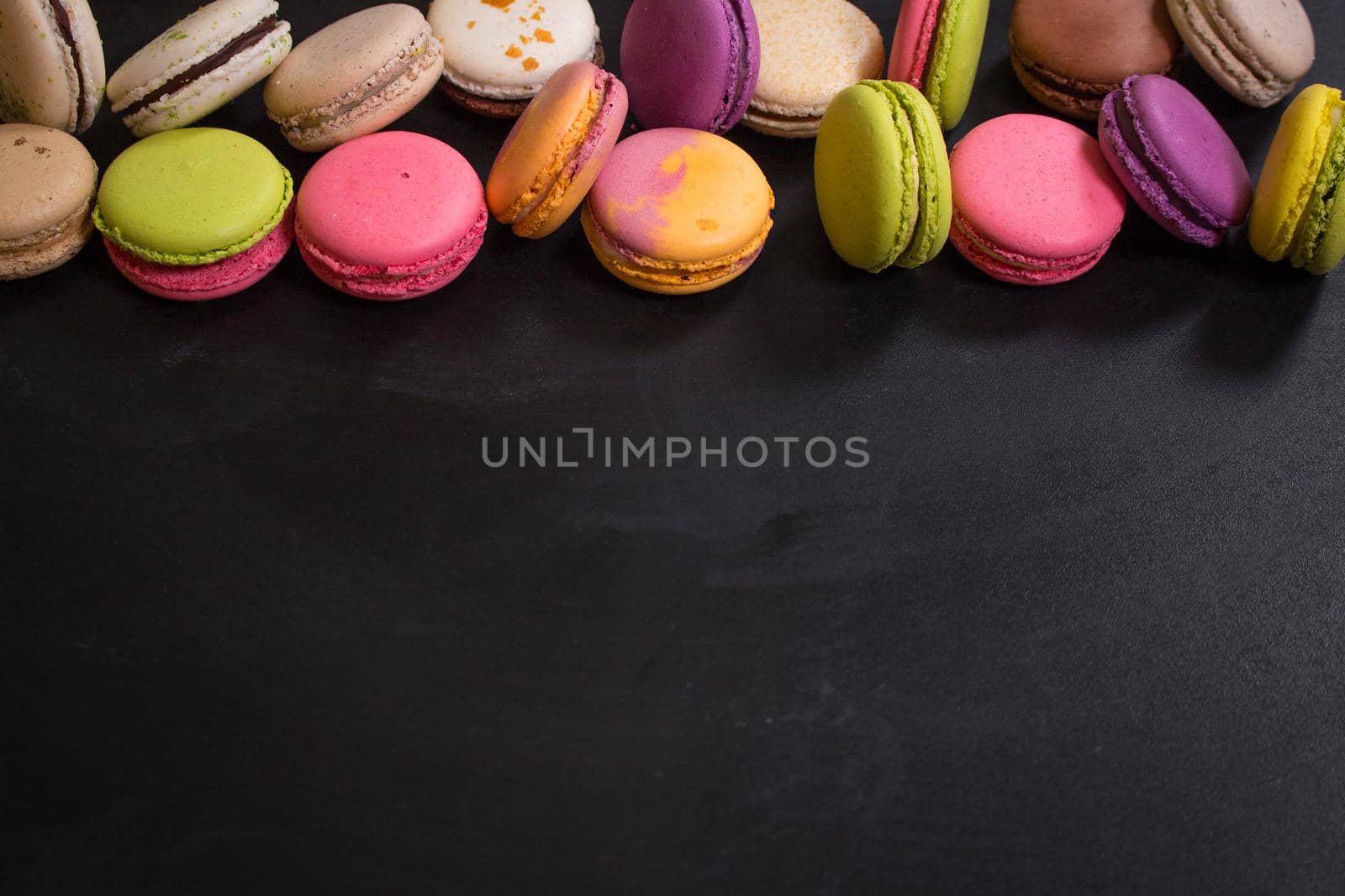 Assorted colorful french cookies macarons on a black background. Space for text. Closeup. Top view. Concept of the baking macarons