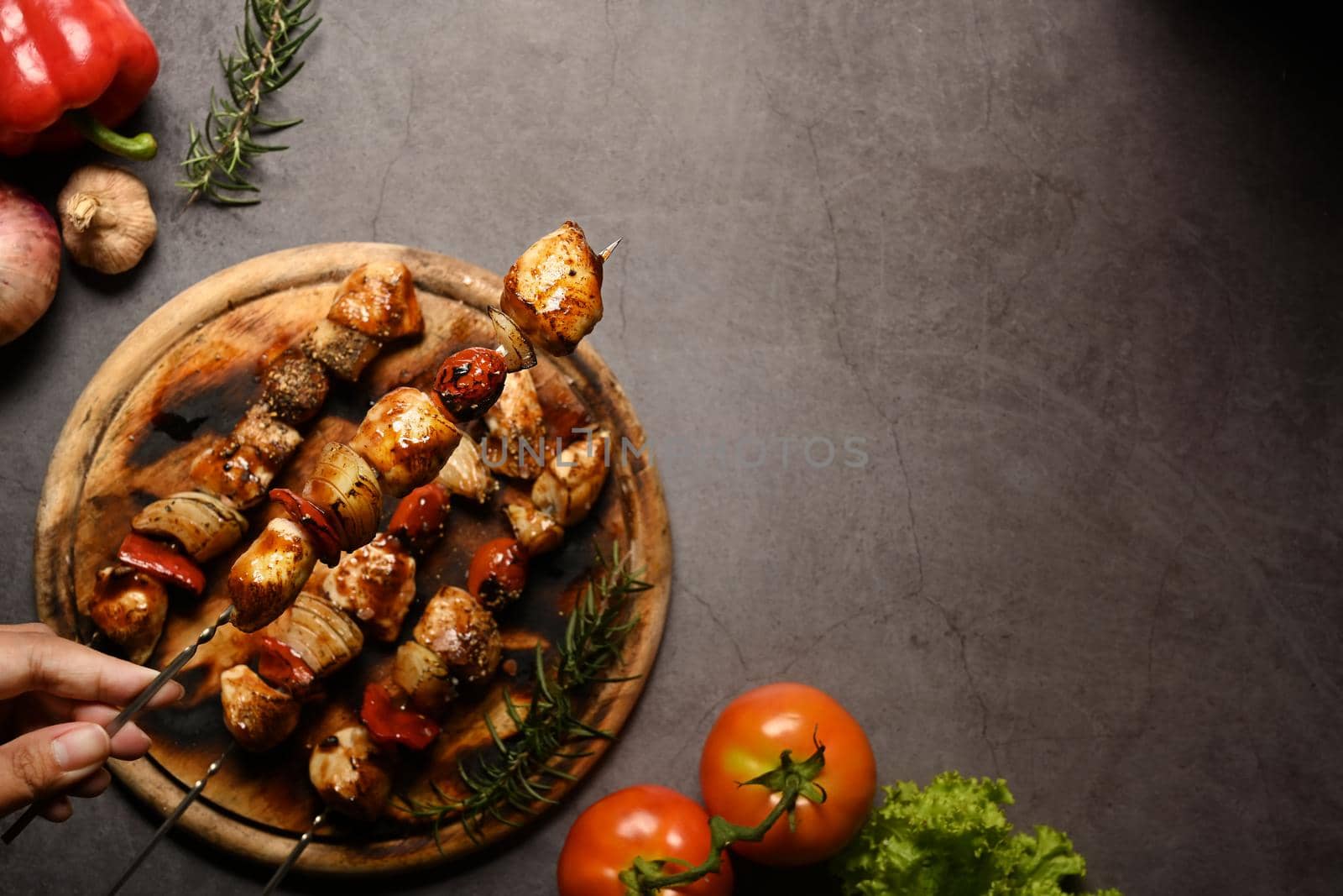 Above view hand holding tasty grilled chicken skewers with tomato, sweet pepper and onions. Copy space for your text.