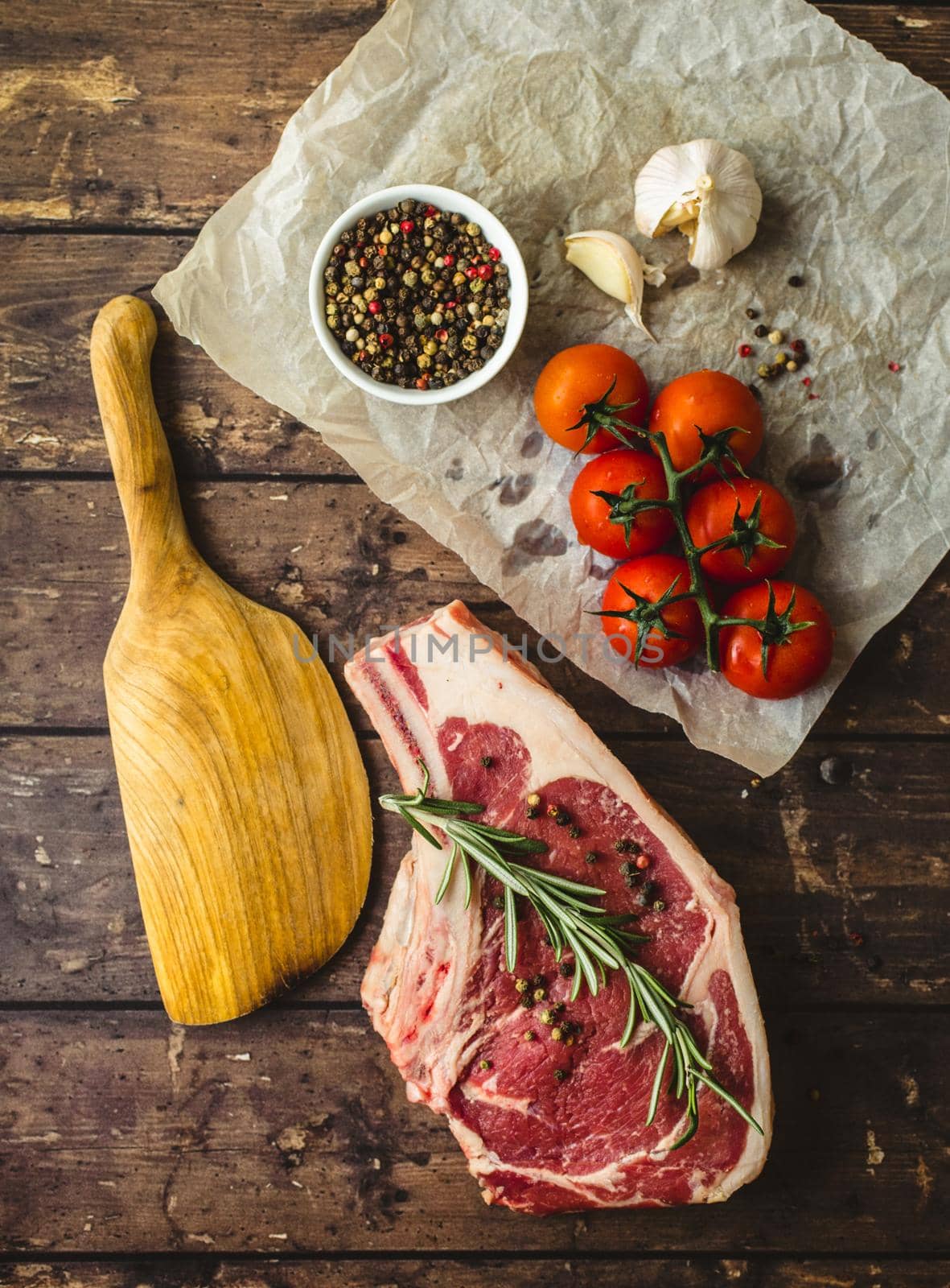 Raw marbled meat steak, pepper, herbs, tomatoes, old wooden table background. Beef Rib eye steak ready for cooking. Top view. Ingredients ready for meat roasting. Uncooked Ribeye meat steak. Closeup