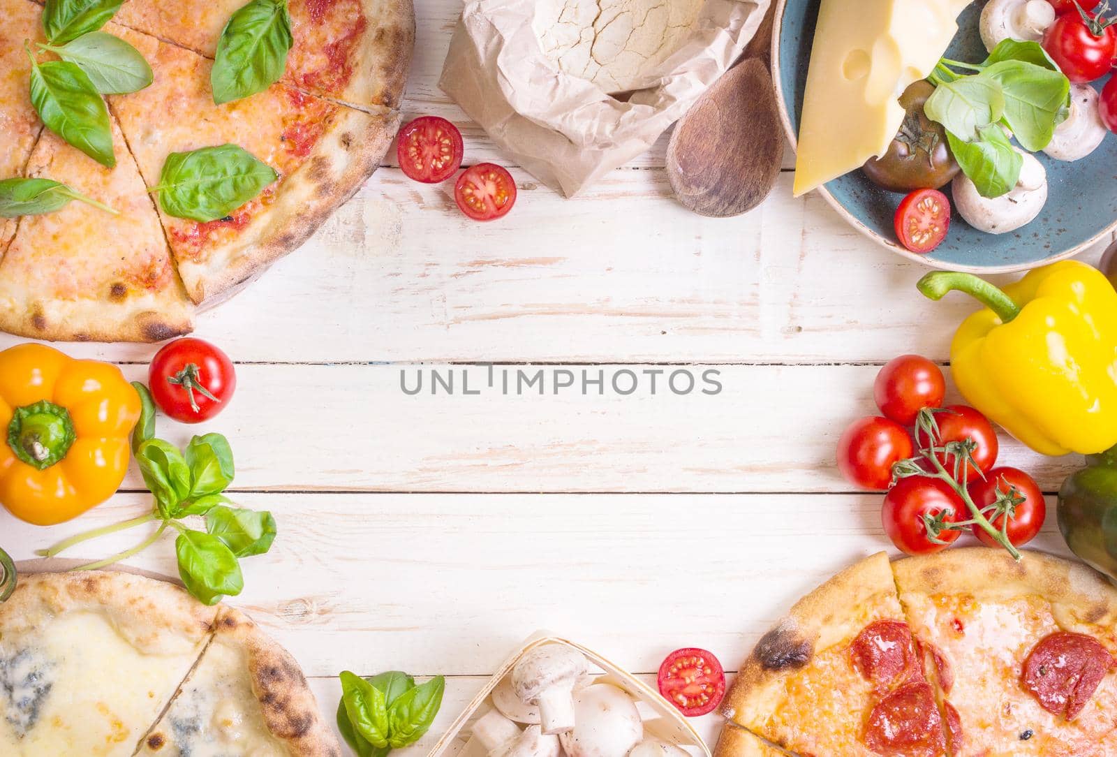 Pizza with assorted toppings and ingredients background. Space for text. Pizza, flour, cheese, tomatoes, basil, pepperoni, mushrooms and rolling pin over white wooden background. Top view. Food frame