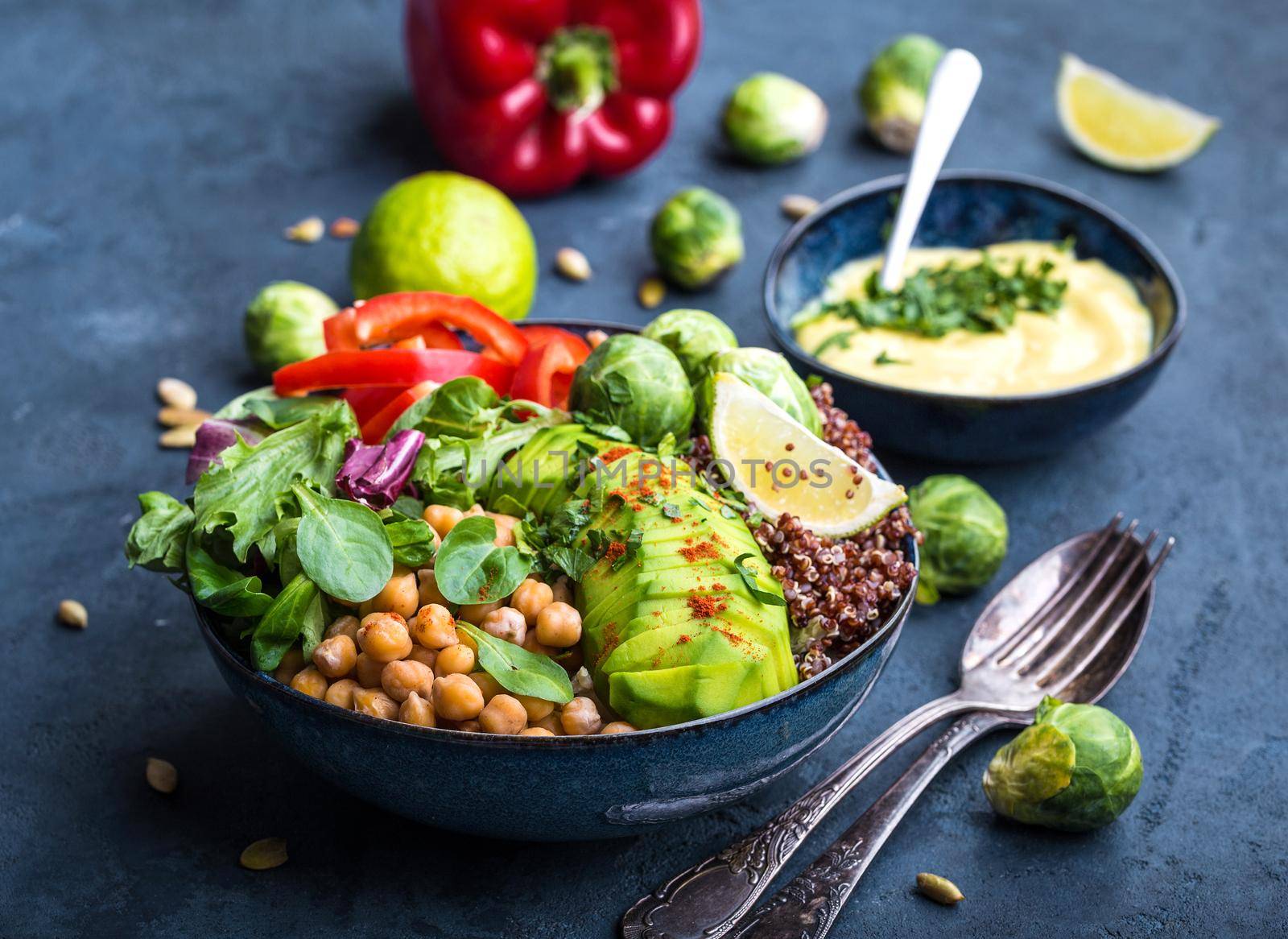 Bowl with healthy salad and dip. Close-up. Buddha bowl with chickpea, avocado, quinoa seeds, red bell pepper, fresh spinach, brussels sprout, lime mix. Vegetarian salad. Clean healthy eating concept