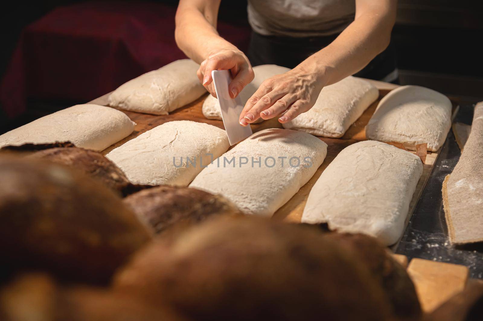 Women's hands carry out actions with raw bread. Dough before dipping into a bakery oven.