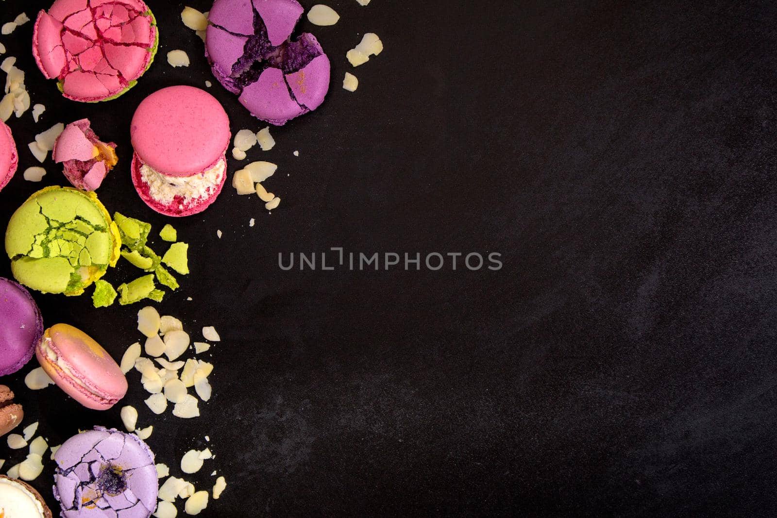 Assorted colorful french macarons and almond flakes on a black background. Space for text. Closeup. Top view. Concept of the baking macarons