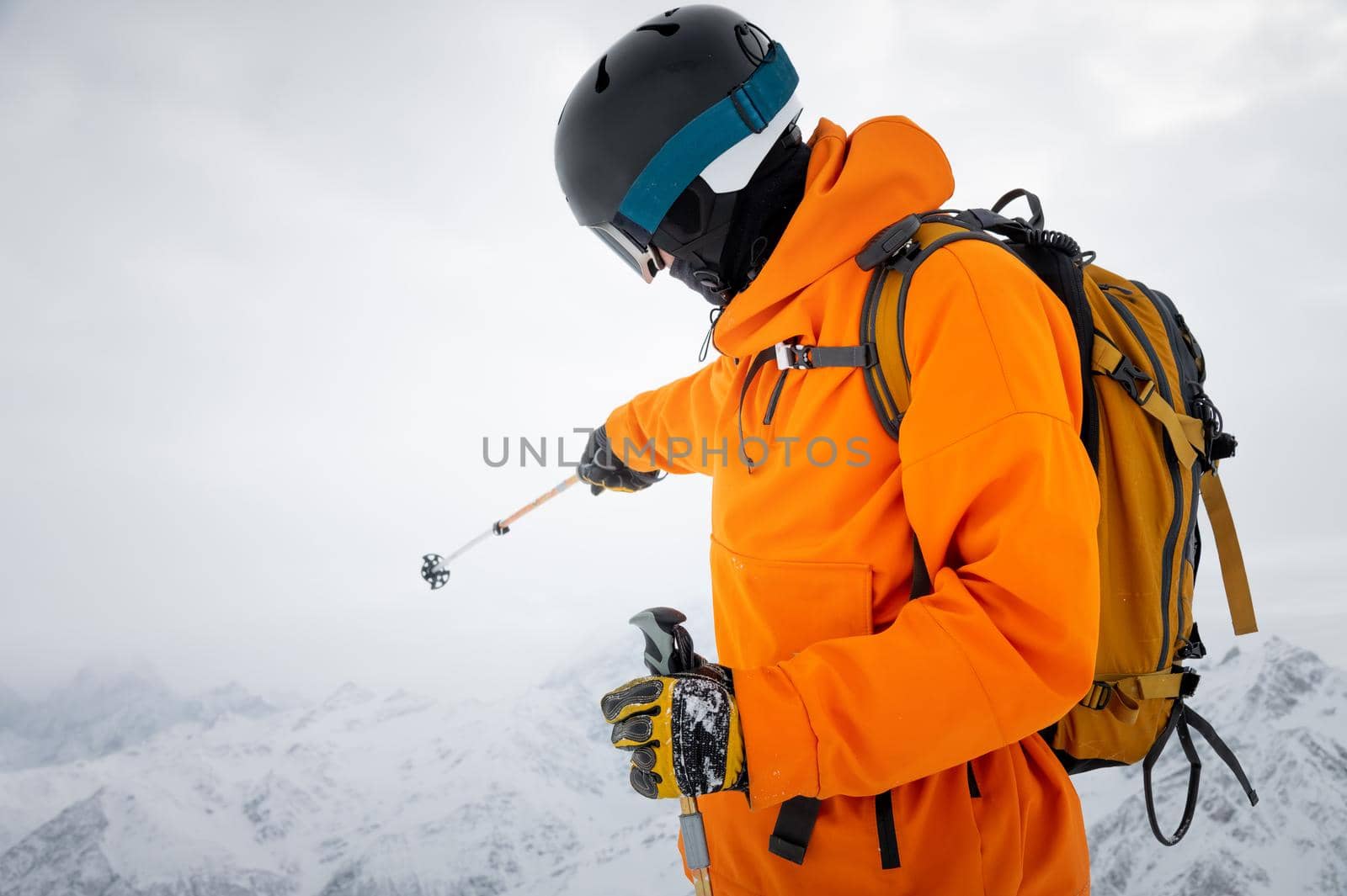 Portrait of a young adult in a ski helmet and goggles, with high snowy mountains in the background.