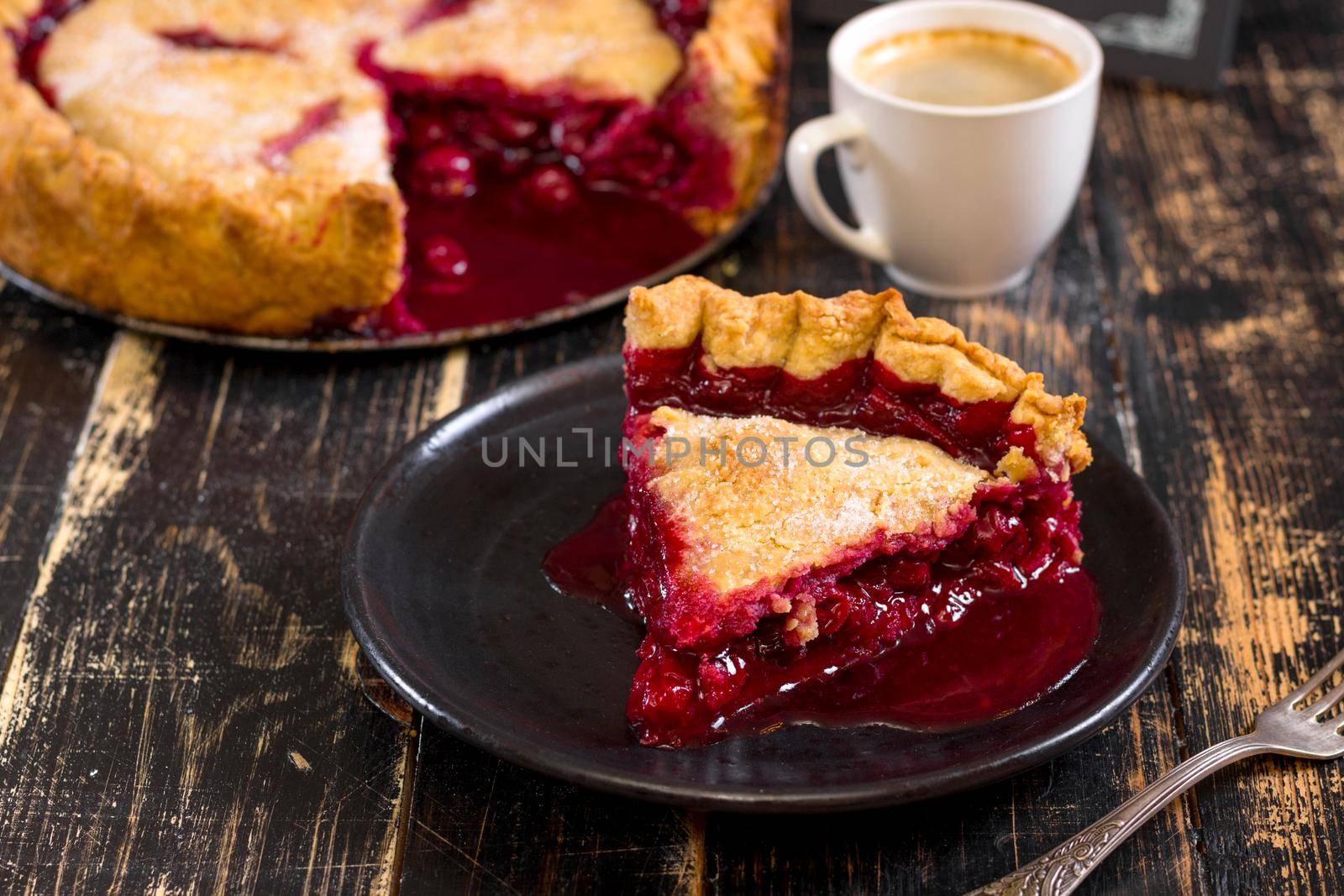 Slice of homemade cherry pie, cup of coffee, bowl with cherries and menu chalkboard on the black wooden table