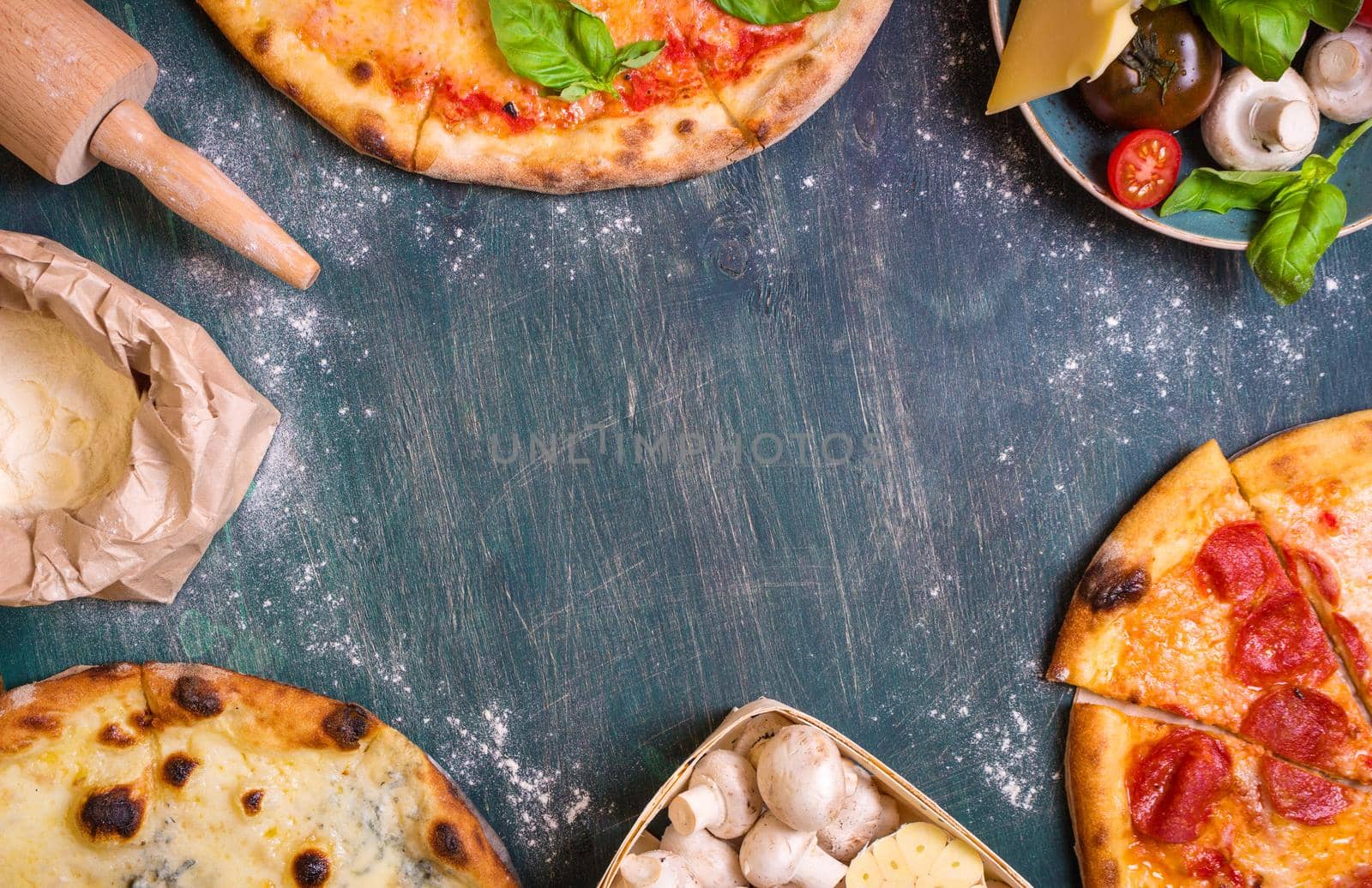 Pizza with assorted toppings and ingredients background. Space for text. Pizza, flour, cheese, tomatoes, basil, pepperoni, mushrooms and rolling pin over old wooden background. Top view. Food frame