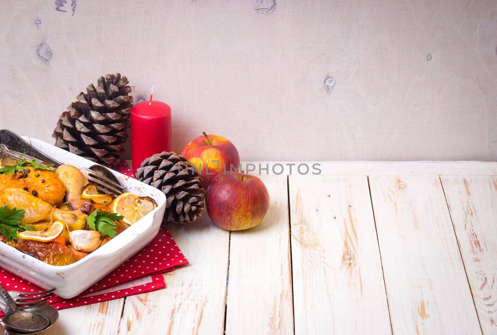 Roasted chicken. Christmas food background. Celebration white wooden table with roasted chicken, apples, decorated with candles, cones, vintage cutlery. Christmas/Thanksgiving dinner. Space for text