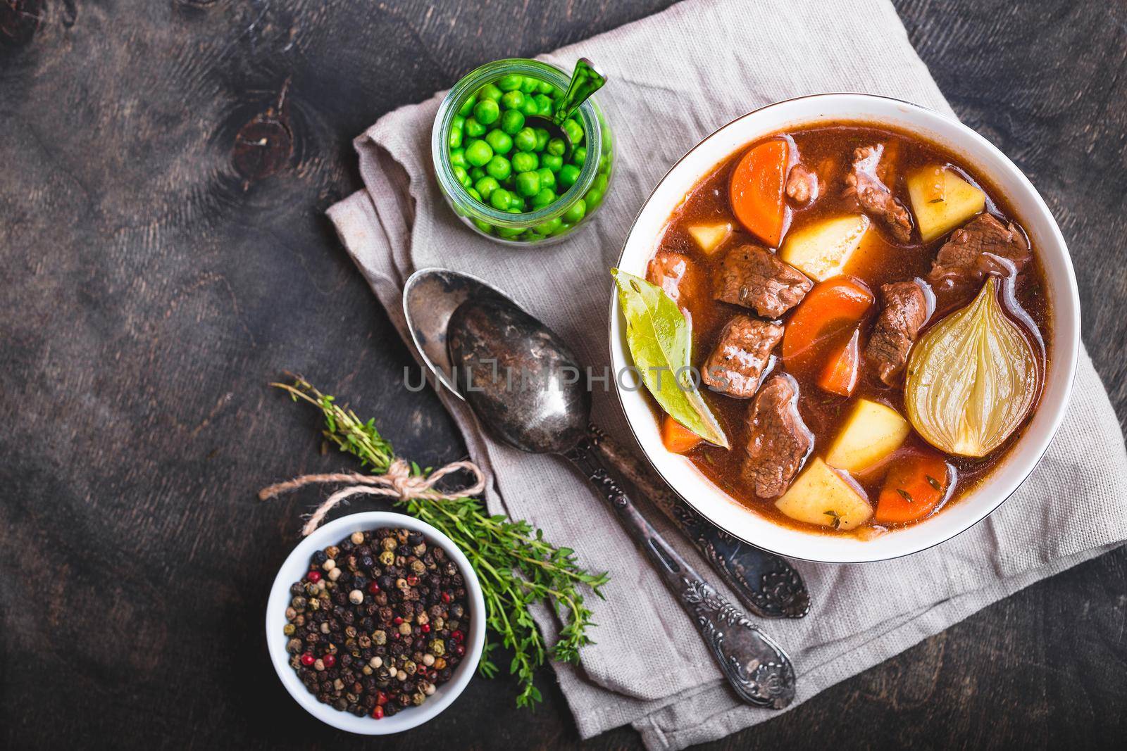 Meat stew with beef, potato, carrot, onion, spices. green peas. Slow cooked meat stew in bowl, wooden background. Hot autumn/winter dish. Closeup. Top view. Space for text. Comfort food. Homemade soup