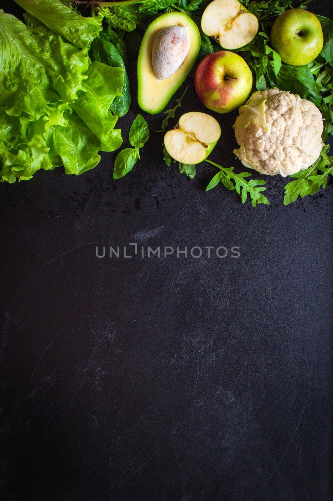 Fresh green vegetables and fruits on black chalk board background. Сauliflower, avocado, spinach, lettuce salad, green apples, herbs. Vegetarian food. Diet/healthy/detox food concept. Space for text