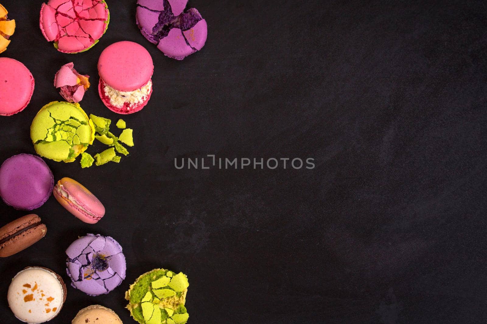 Assorted colorful french macarons on a black background. Space for text. Closeup. Top view. Concept of the baking macarons