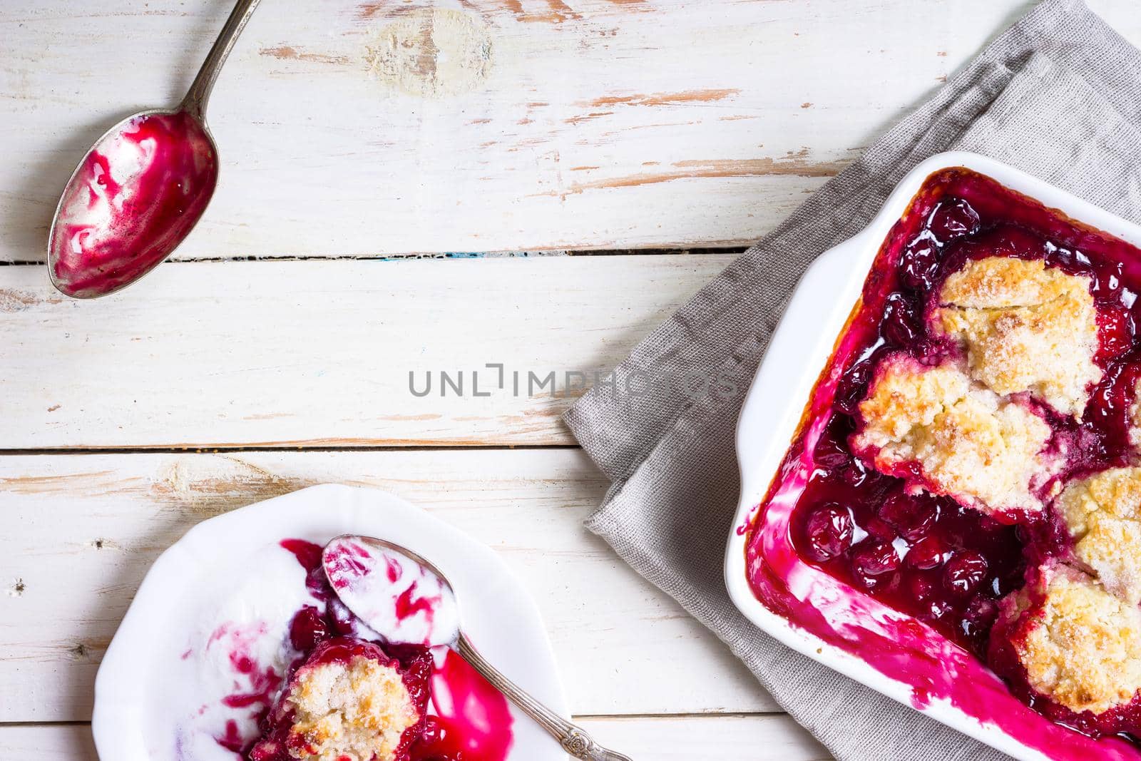 Homemade cherry cobbler pie with flaky crust, ice cream, vintage spoon, sieve for flour. Top view on the white wooden table background. Space for text