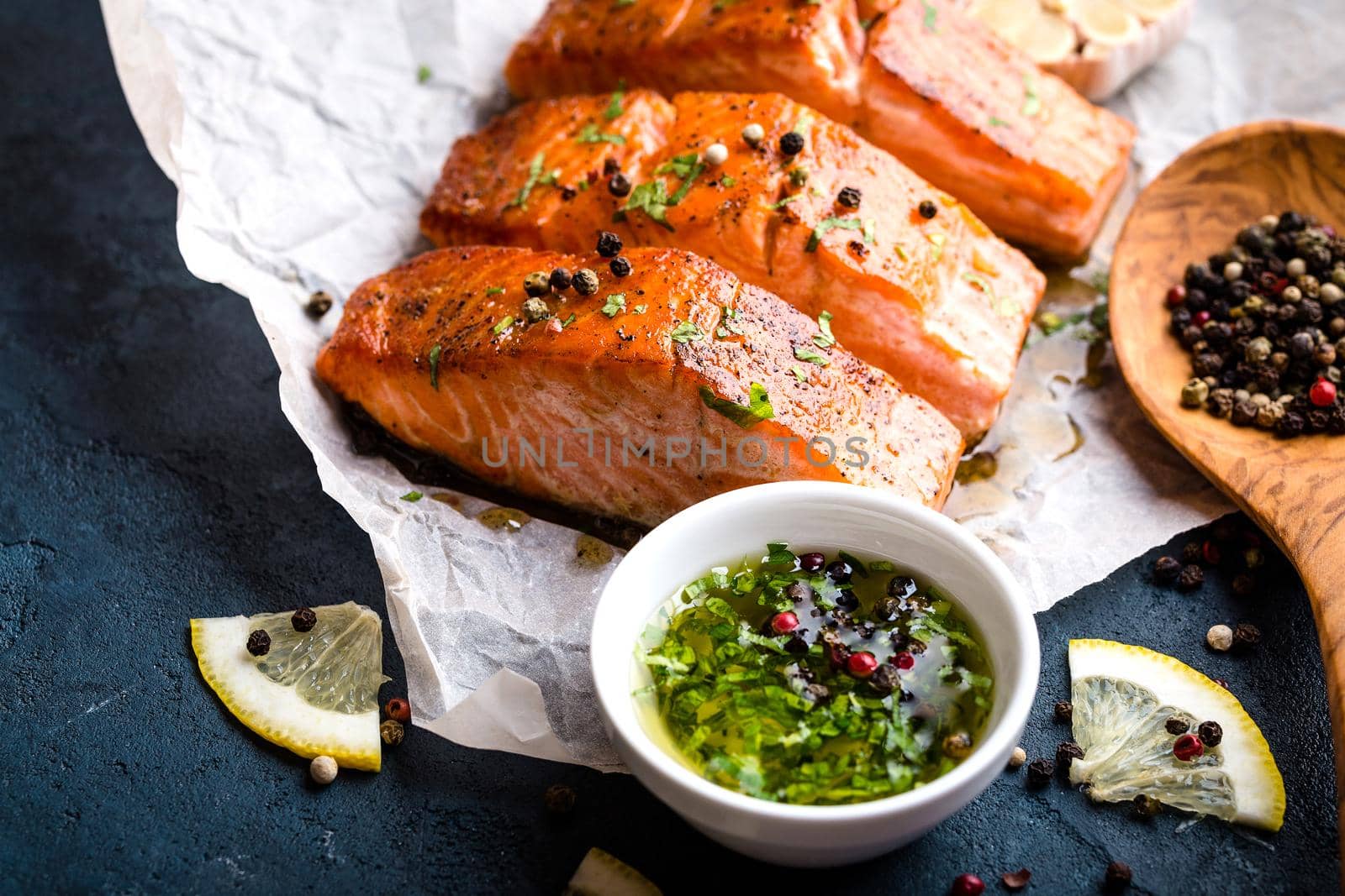 Delicious fried salmon fillet, seasonings on blue rustic concrete table. Cooked salmon steak with pepper, herbs, lemon, garlic, olive oil, spoon. Grilled fresh fish. Fish for healthy dinner. Close-up