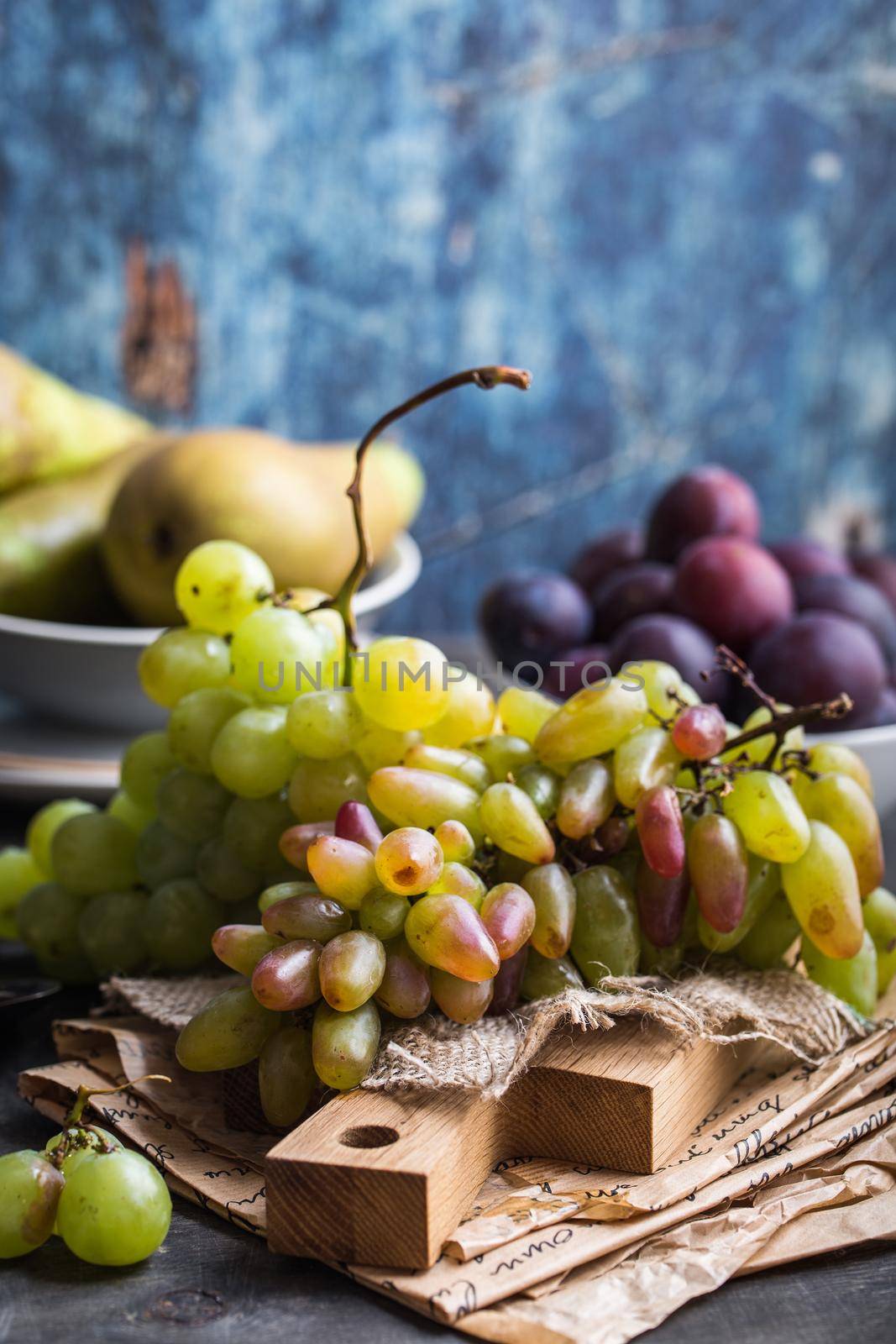 Fresh ripe grapes on wooden cutting board, pears and plums in bowls, wooden rustic background. Fresh juicy organic fruits. Close up. Organic natural fruits. Autumn/fall setting. Harvest/crop/garden