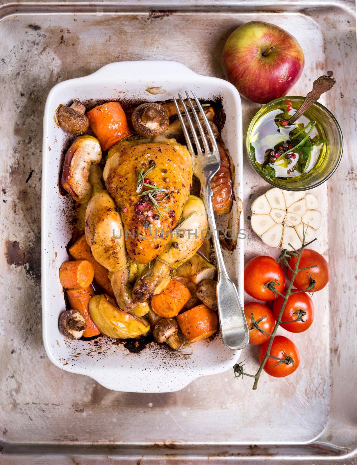 Delicious baked juicy chicken with golden crispy skin. Roasted chicken in baking dish with apples, carrot, mushrooms, rosemary, garlic, pepper on iron oven-tray. Overhead. Dinner. Prepared poultry