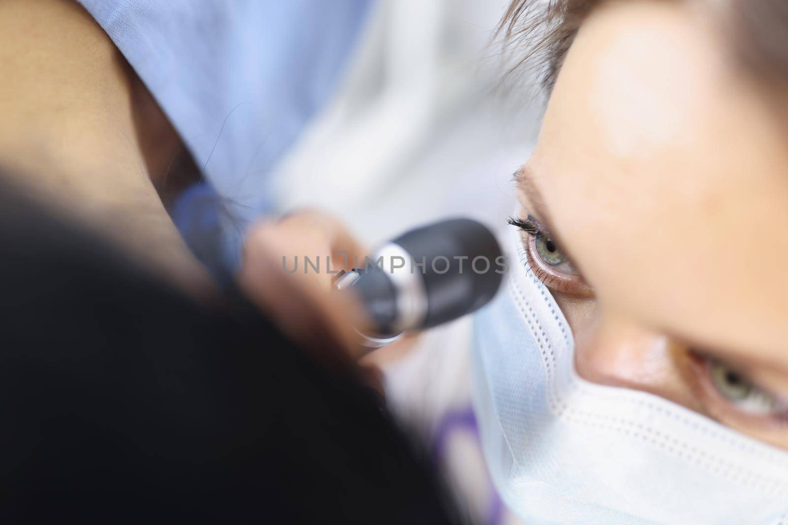 Top view of female ent doctor in medical mask examining ear with otoscope carefully. Patient at practitioner appointment. Otolaryngology, medicine and healthcare concept