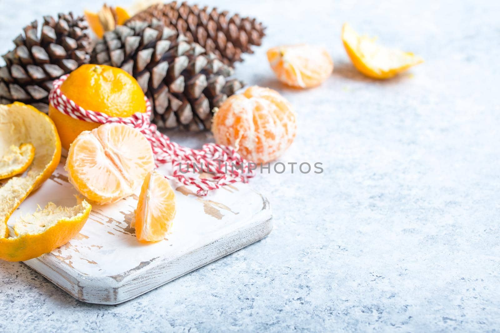 Winter white christmas background, tangerines, pine cones. Peeled tangerine, white cooking board. New Year/Xmas festive background. Winter holidays. Decoration, celebration Christmas. Space for text