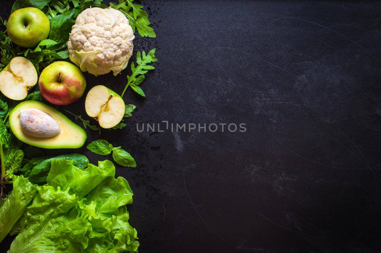 Fresh green vegetables and fruits on black chalk board background. Сauliflower, avocado, spinach, lettuce salad, green apples, herbs. Vegetarian food. Diet/healthy/detox food concept. Space for text