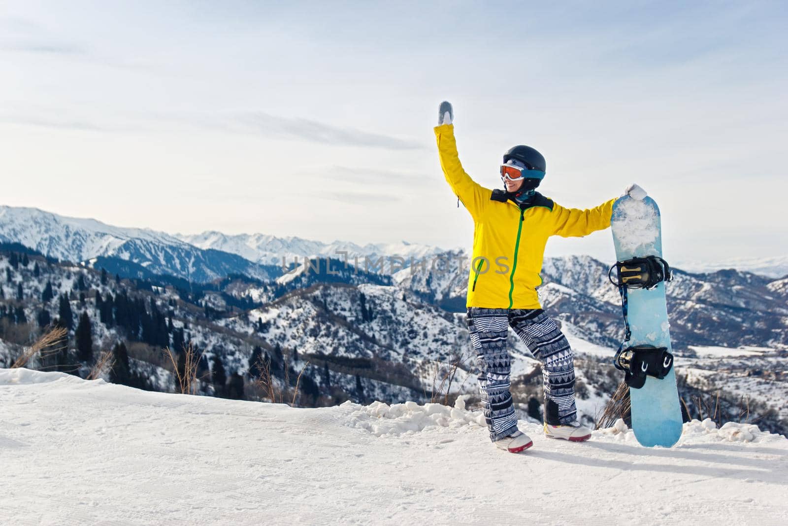 Young woman snowboarder in a yellow jacket and black helmet on the background of snowy mountains