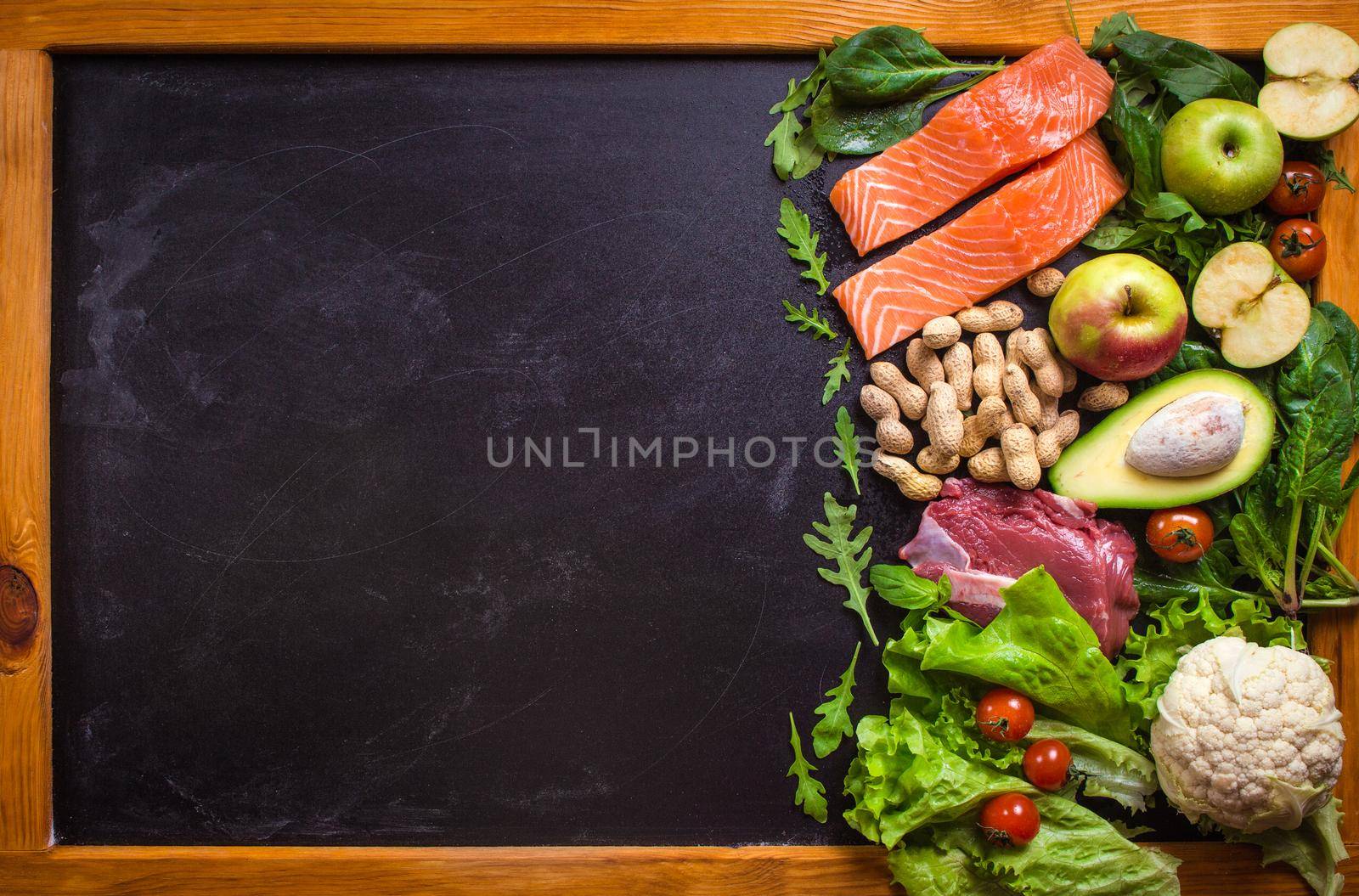 Fresh vegetables, fruits, fish, meat, nuts on black chalk board background. Сauliflower, avocado, apples, tomatoes, salmon, beef, spinach, herbs. Diet/healthy/paleo food. Ingredients. Space for text