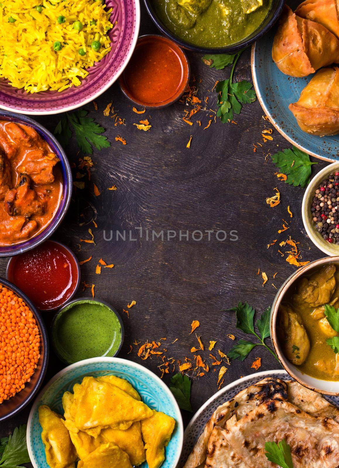 Assorted indian food on dark wooden background. Dishes of indian cuisine. Curry, butter chicken, rice, lentils, paneer, samosa, naan, chutney, spices. Space for text. Bowls and plates with indian food