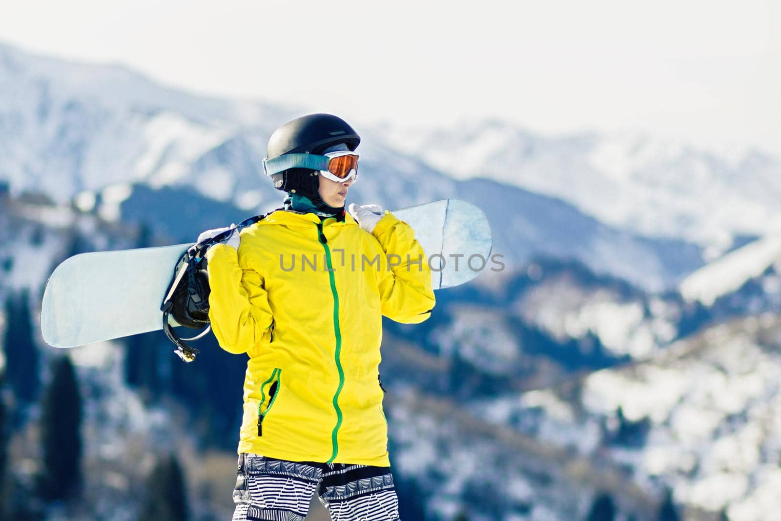 Young woman snowboarder with snowboard on her shoulders looks at the at the ski slope, copy space